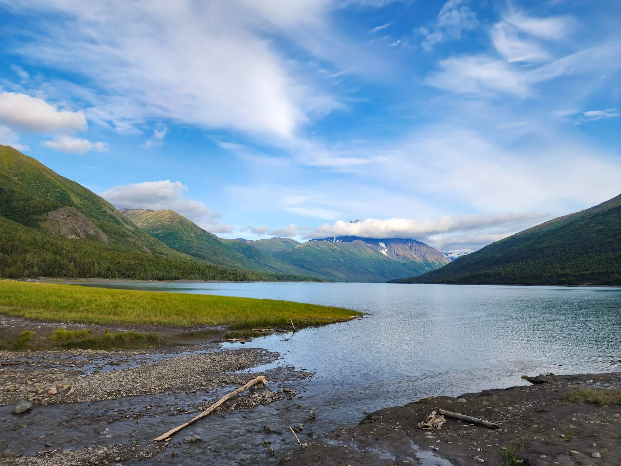 View of Eklutna Lake from the shore on a sunny day with one low cloud lingering over the mountain in the distance.