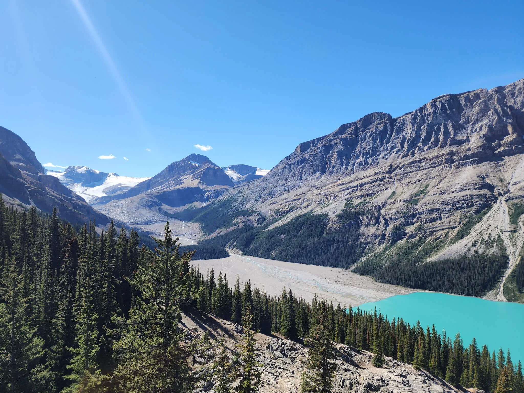 View of giant mountains with a glacier in the background and a bright blue glacier fed lake below.