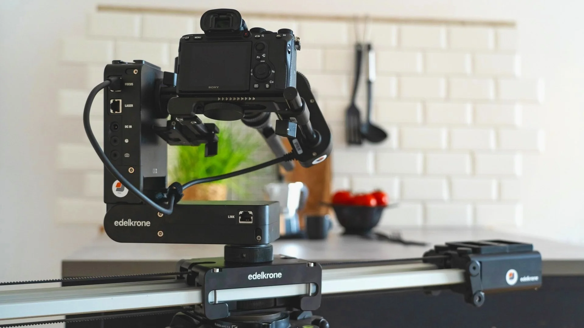 Produktionsküche | Vorbereitungsküche in Köln | Kameratechnik auf einem Slider in einer modernen Küche, Hintergrund mit weißen Fliesen, woraus einige Küchenutensilien und eine Schüssel mit roten Tomaten sichtbar sind.