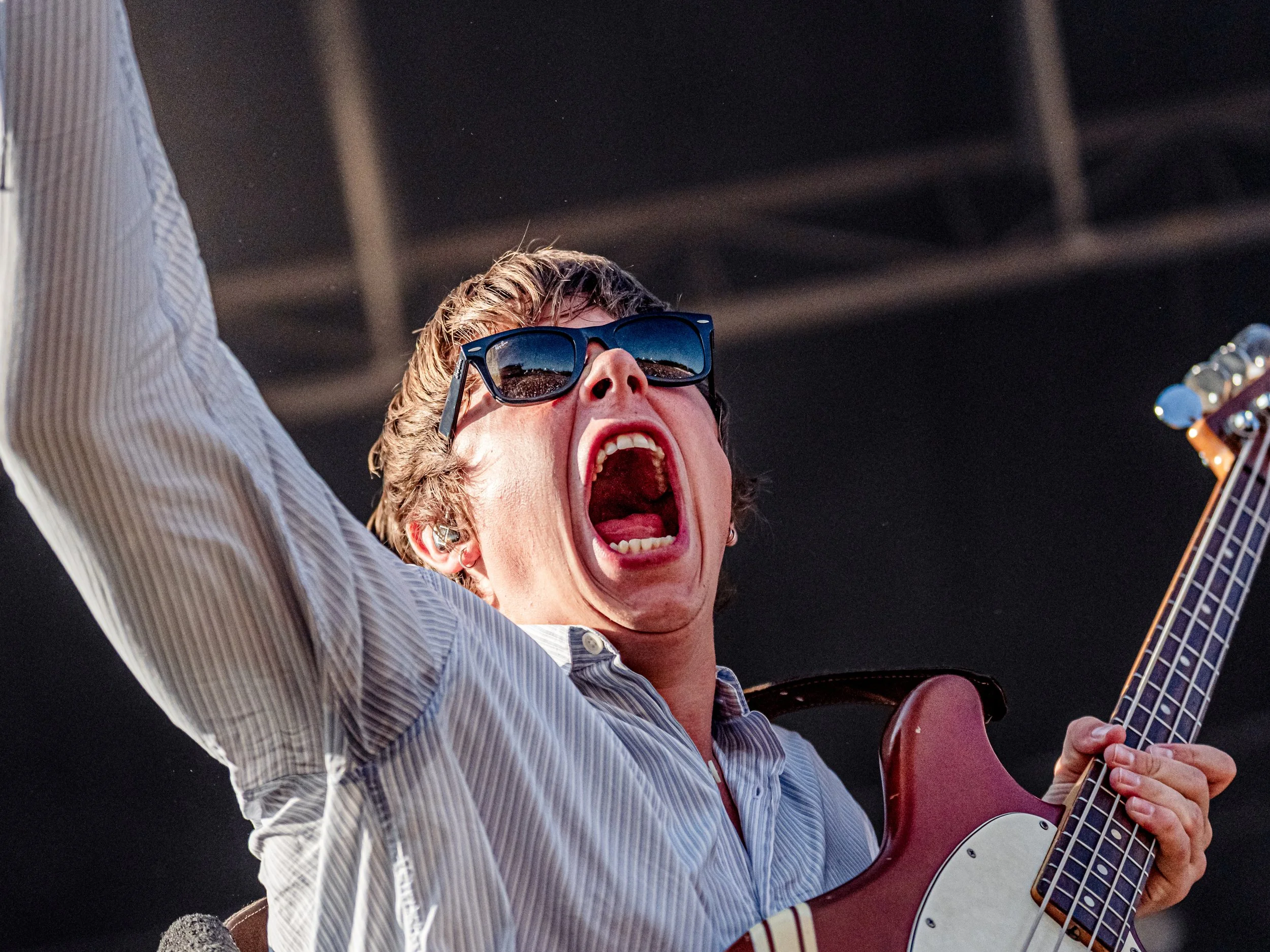 En person med sunglasses spiller guitar og synger med åbent mund.
