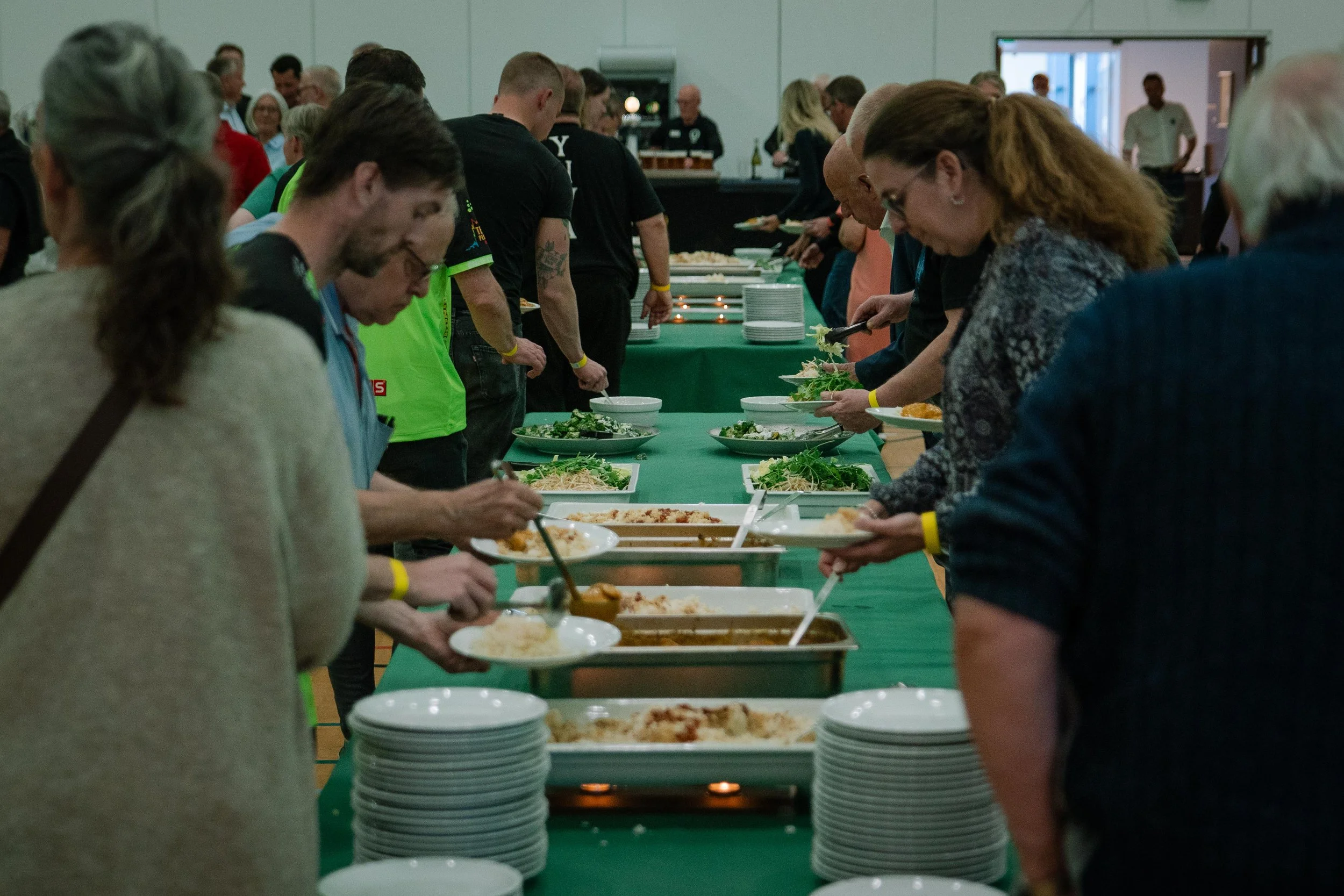 Folk står i kø for at tage mad fra en buffet med forskellige retter, i en stor konferencehal.