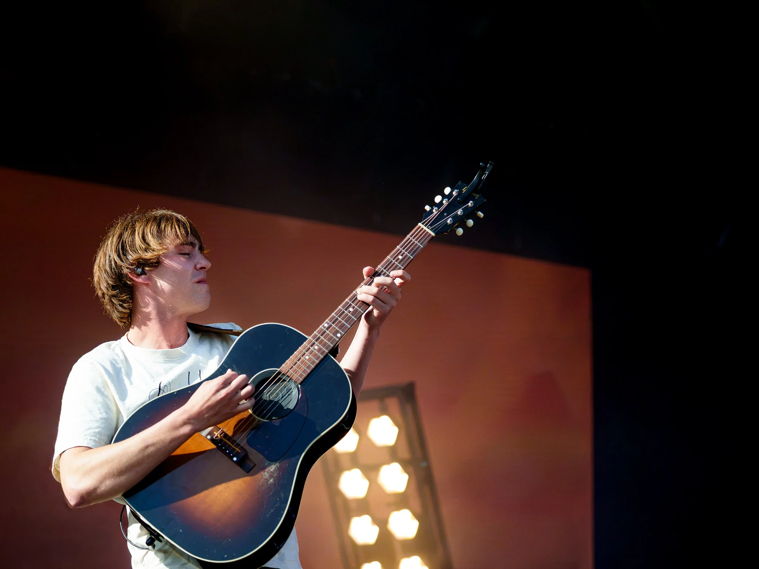 En ung mand spiller på en sort akustisk guitar på scenen under en koncert.