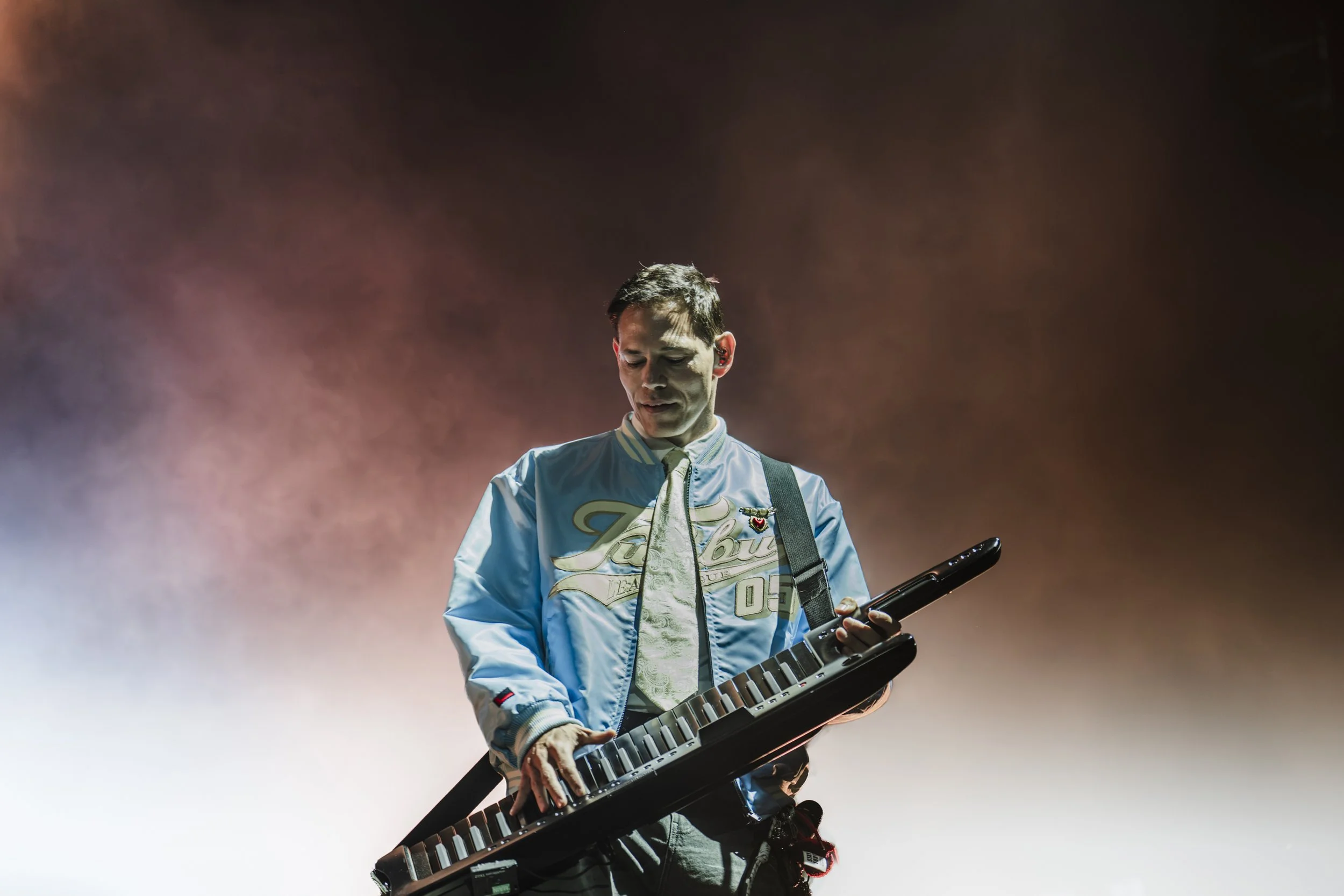 En mand spiller på en synthesizer mod en mørk baggrund.