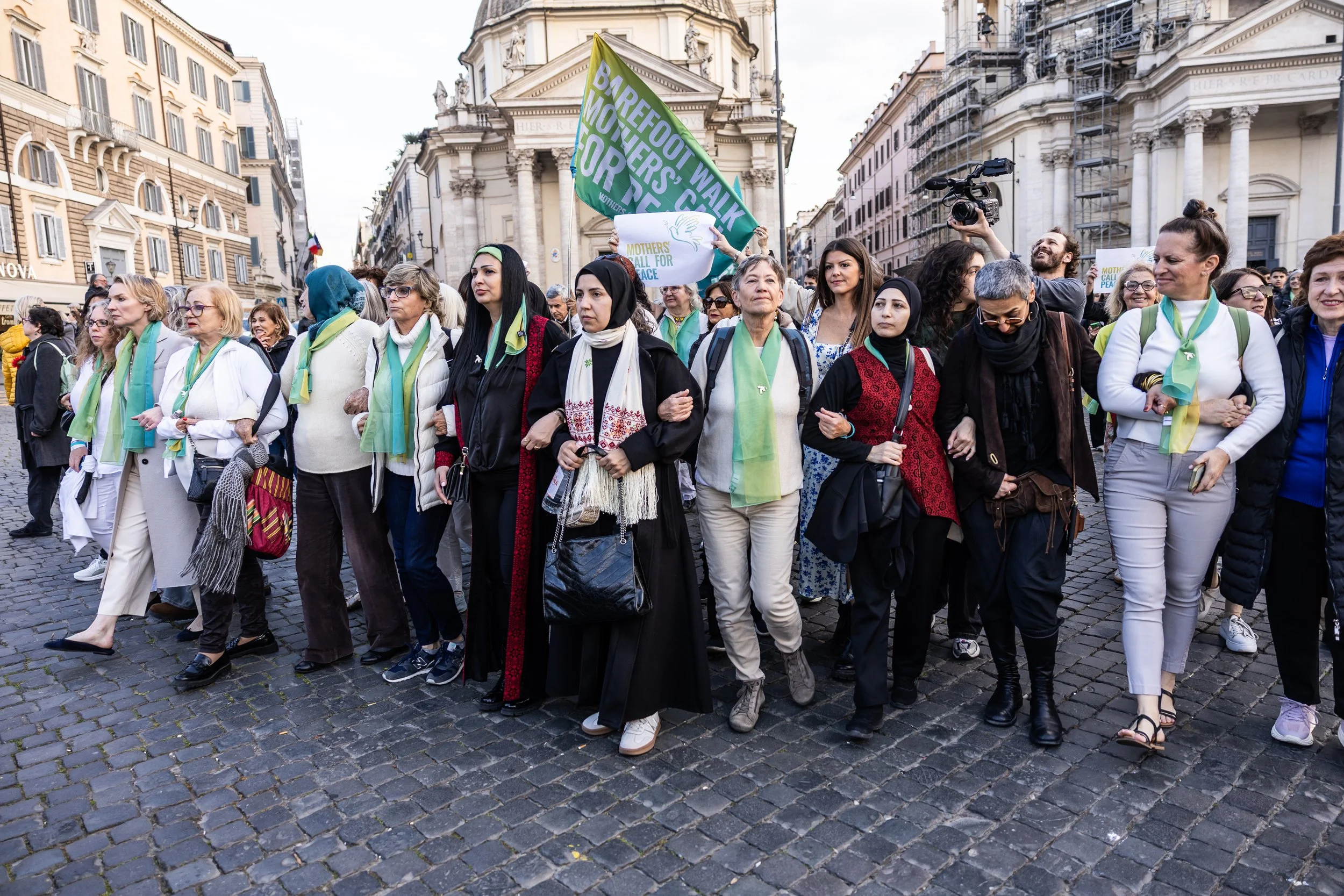 A diverse group of women marching in a protest or rally on a city street, holding flags and signs.