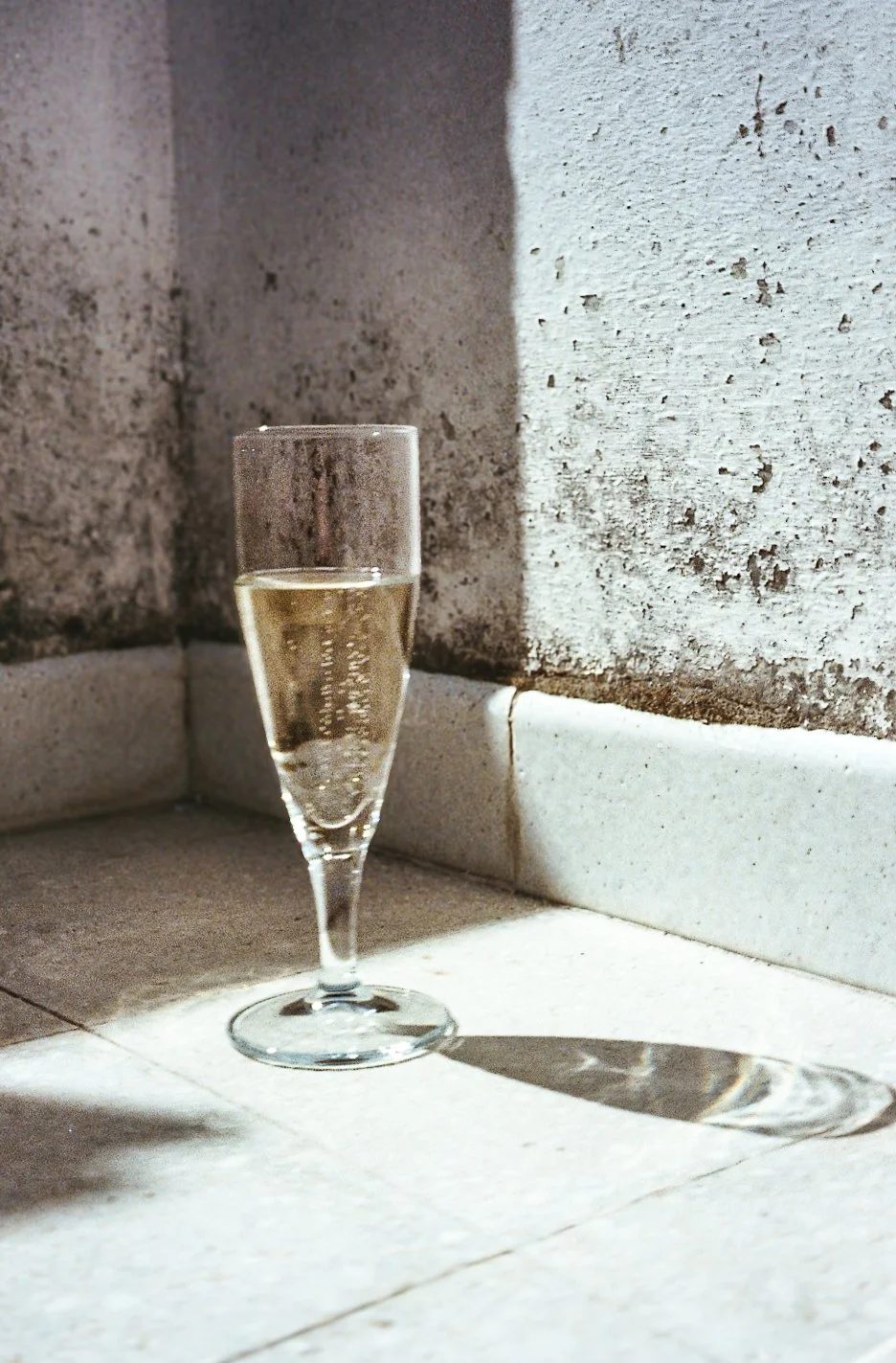 Glass of sparkling wine or champagne on a tiled corner with sunlight casting a shadow.