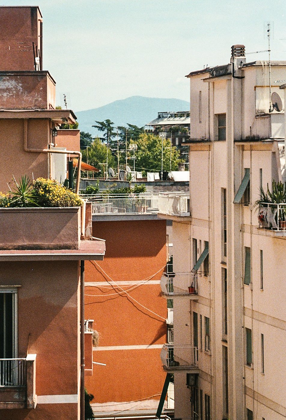 View of apartment buildings with balconies and plants, clotheslines, and a mountain in the background.