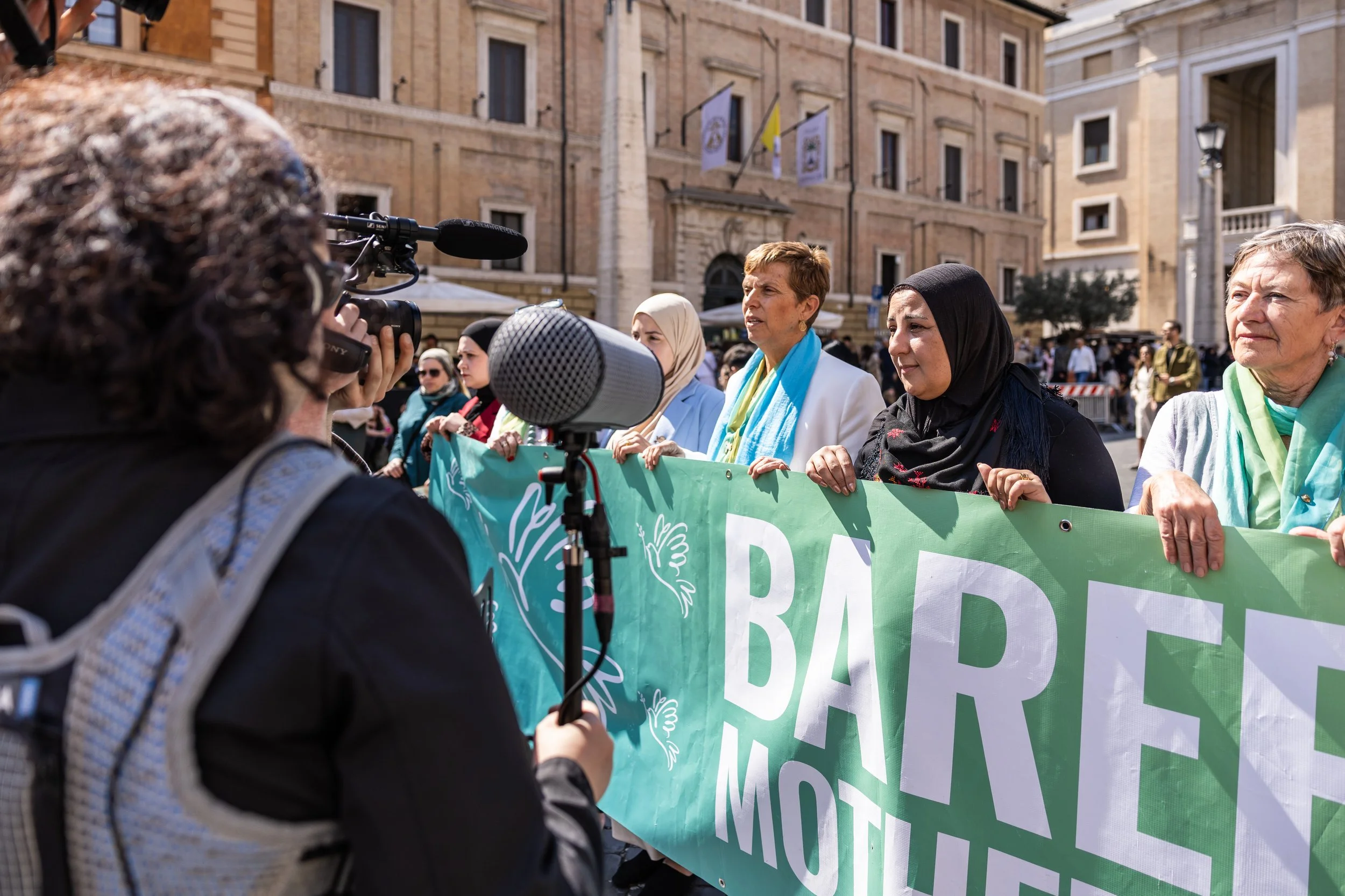 Group of women holding a green banner during a protest or demonstration on a city street with buildings and flags in the background.