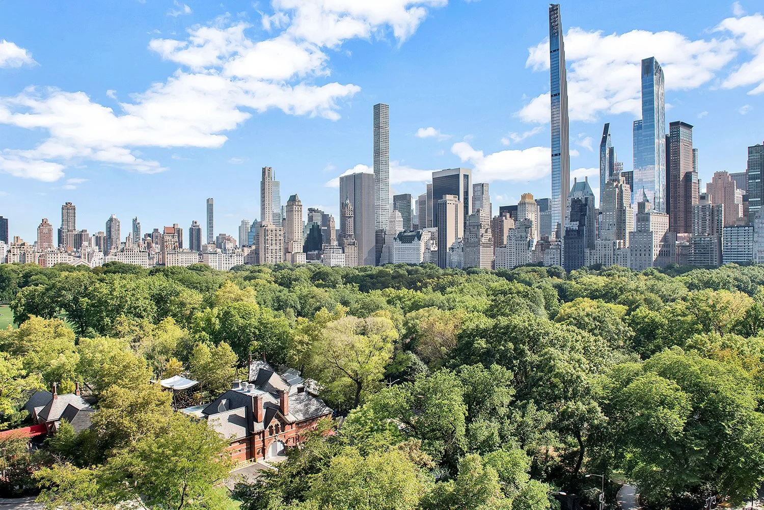 View of a city skyline with tall skyscrapers in the background and a large green park with trees in the foreground on a clear day.