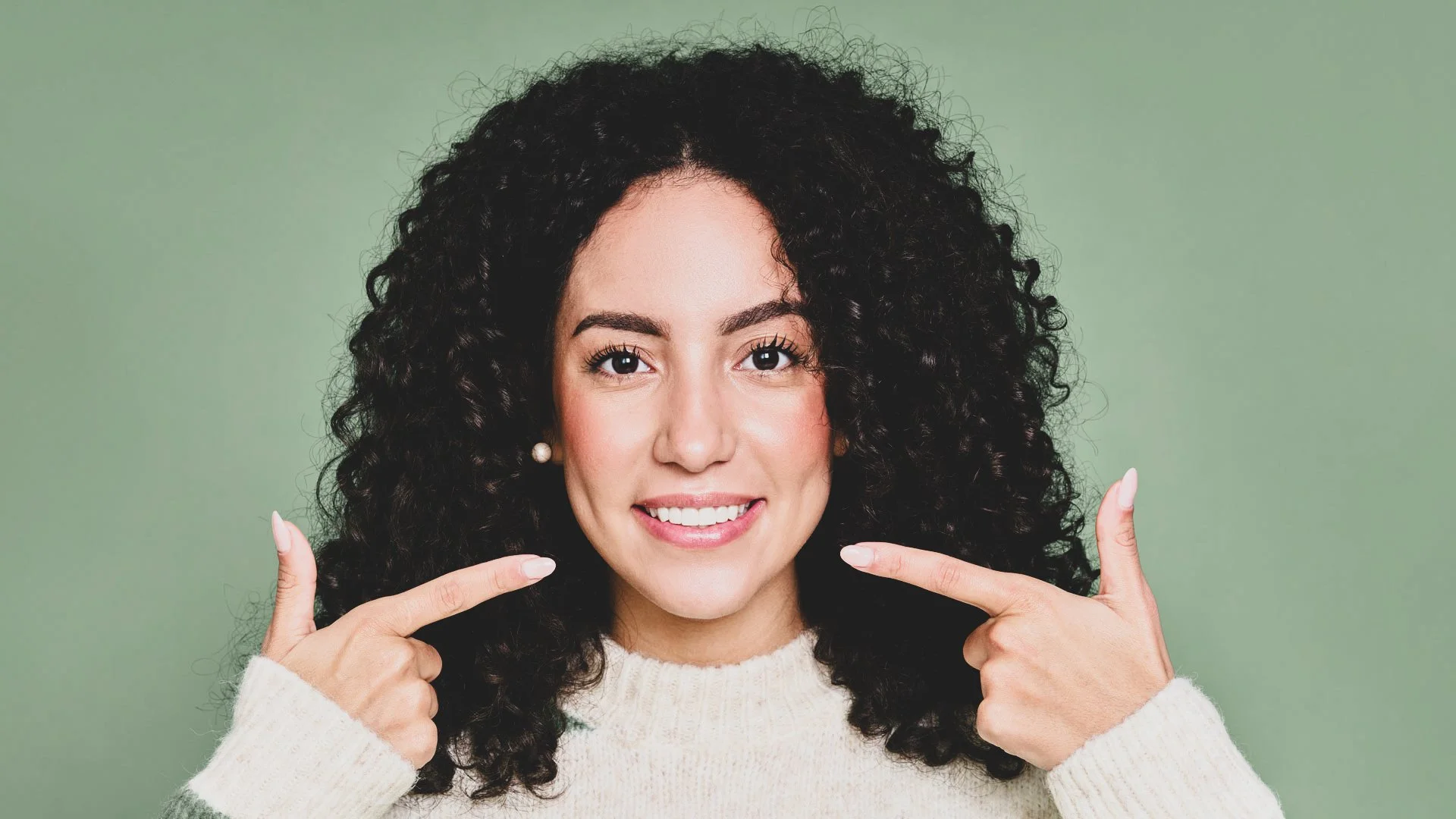 Banner publicitario de una mujer sonriendo y señalando sus dientes. Invitación a recuperar la confianza al comer agendando una evaluación integral de alta complejidad para tratar la pérdida o desgaste dental en Pineda Dental Studio, Recoleta-caba.