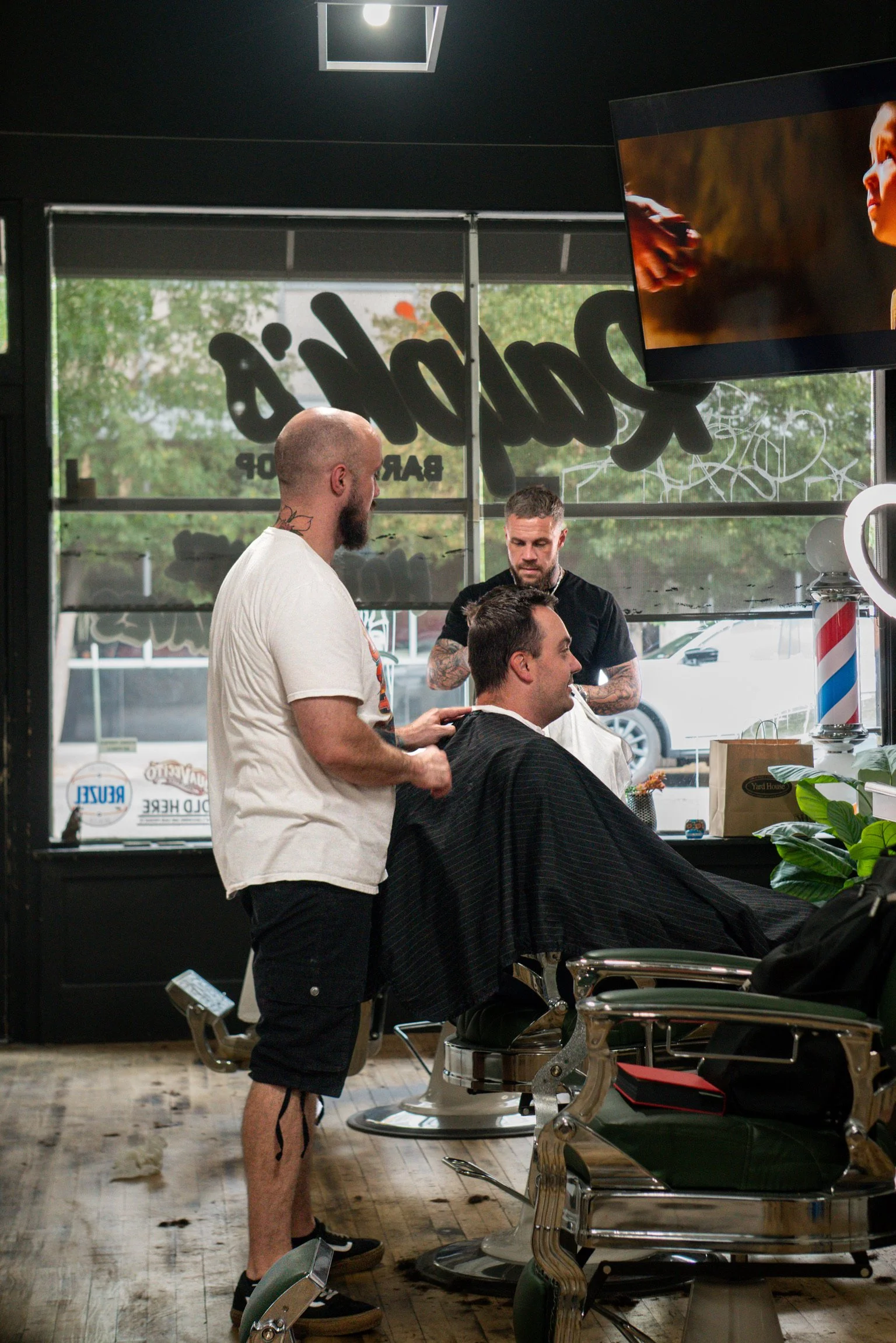 Tony standing behind customer in barber chair. Ralph in the background cutting customer's hair.
