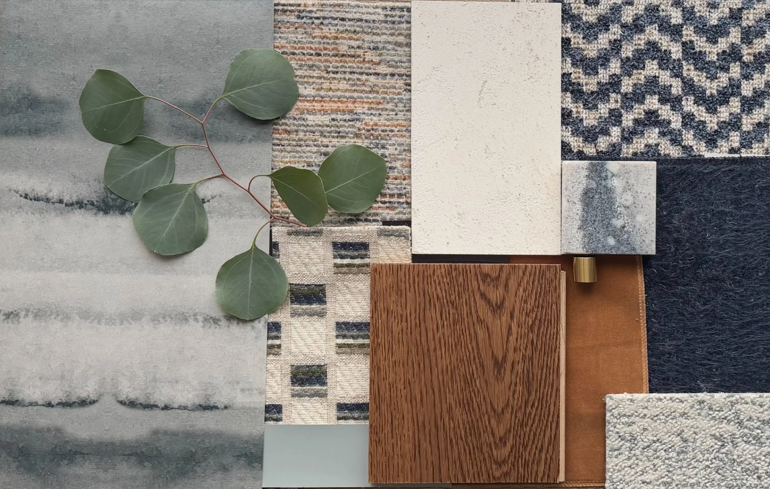 Flat lay of interior design material samples including navy checkered woven fabric, dark navy wool. cream boucle, cognac velvet with brass hardware, warm oak wood, quartz stone, striped and plaid woven textiles, grey marbled wallpaper, and a branch.