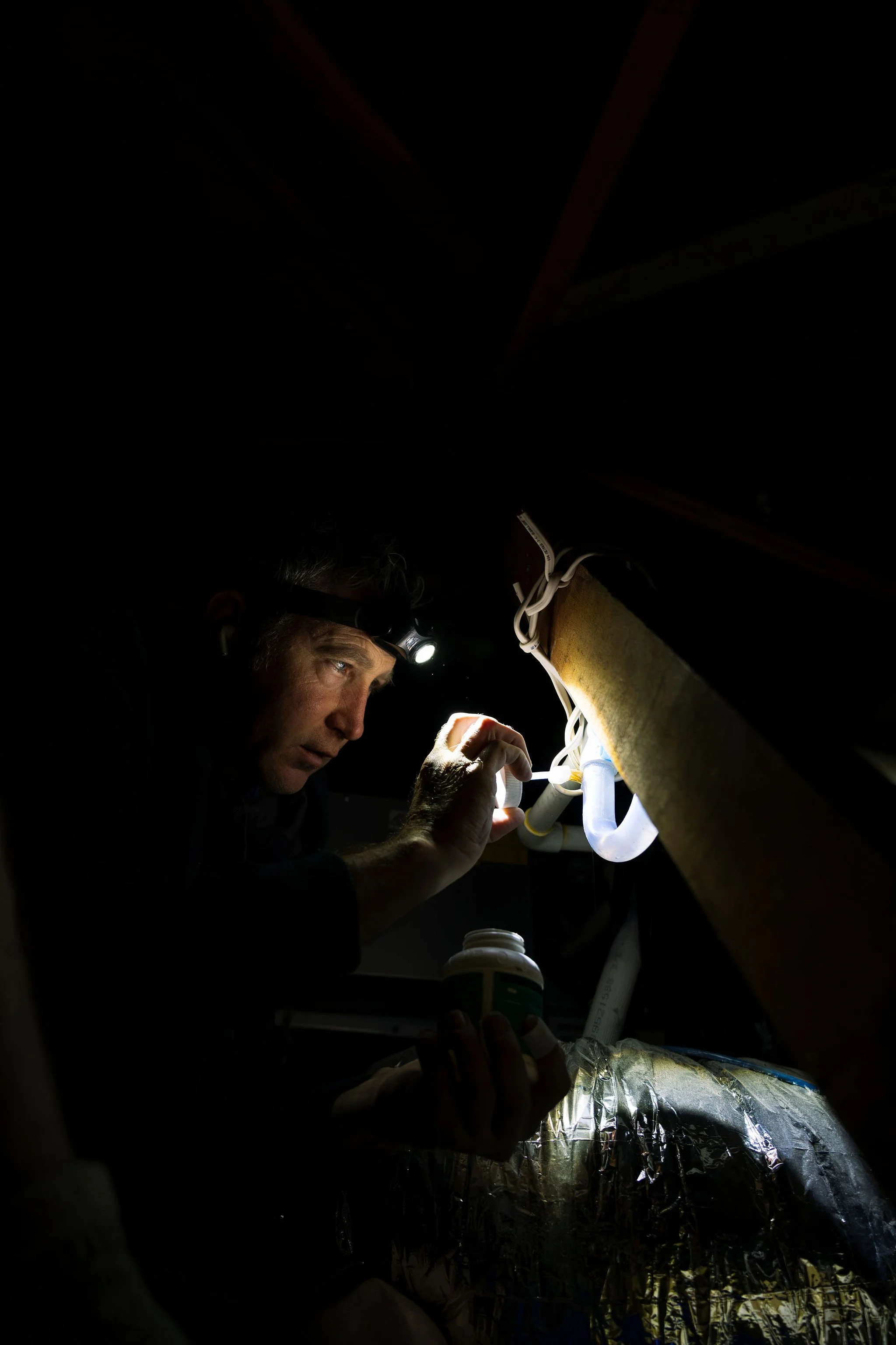 Electrician checking wiring in a ceiling space with a torch