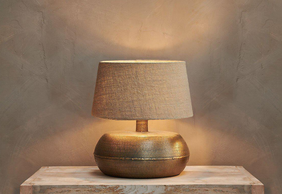 A table lamp with a textured base and shade on a wooden surface against a beige wall.