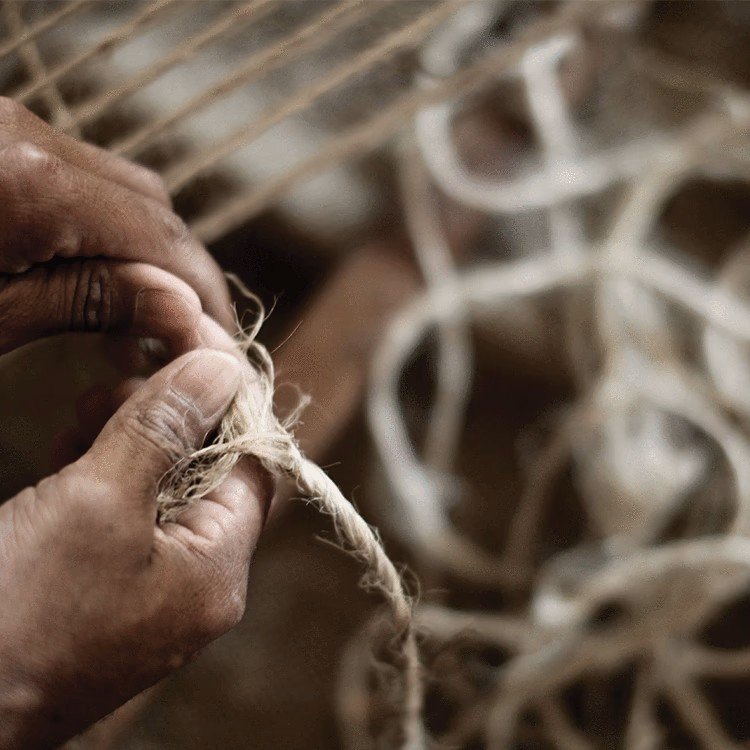 Close-up of hands tying a knot in a piece of rough, beige rope with a woven pattern in the background.