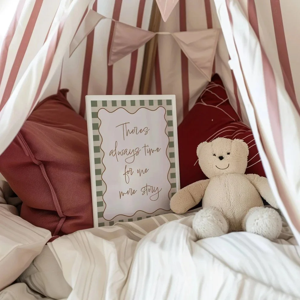 A cozy indoor space with striped pink and white tent-like fabric ceiling, pink pillows, a plush teddy bear, and a framed sign with a decorative border that reads, "There's always time for one more story."