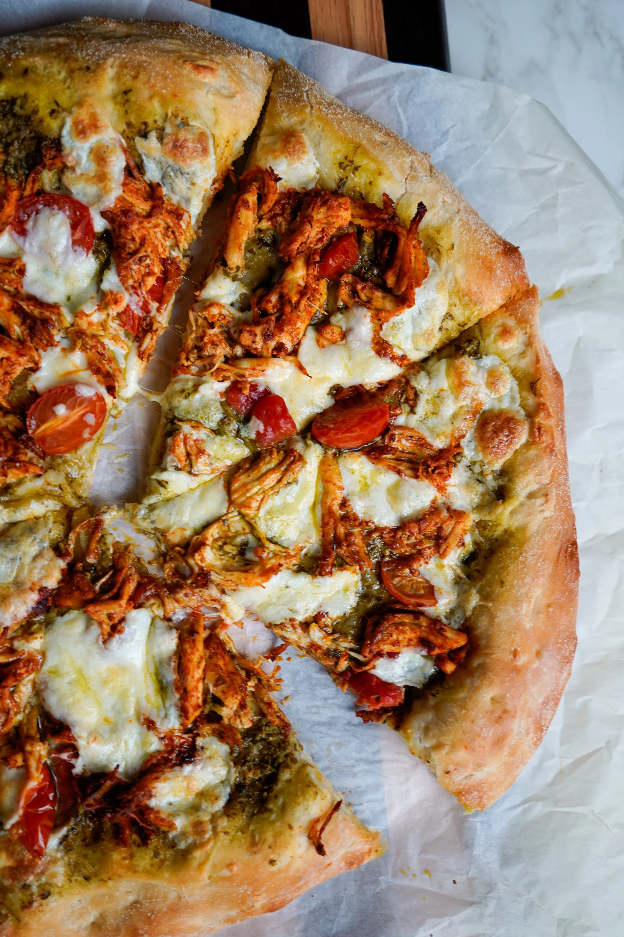 Slice of pizza with cheese, cherry tomatoes, and shredded chicken on a piece of parchment paper.
