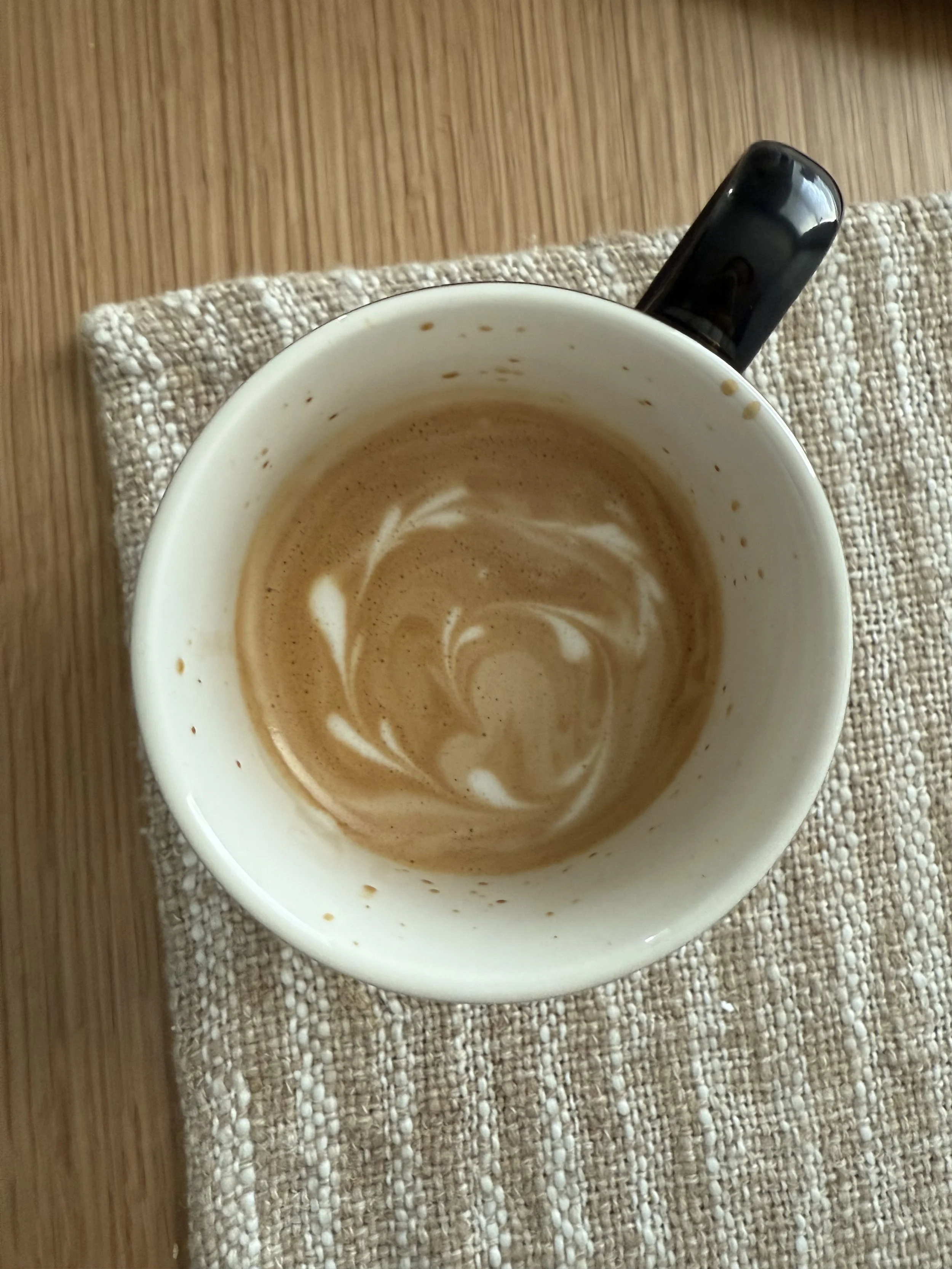 A coffee mug with remnants of coffee and latte art swirl inside, resting on a textured beige placemat on a wooden surface.