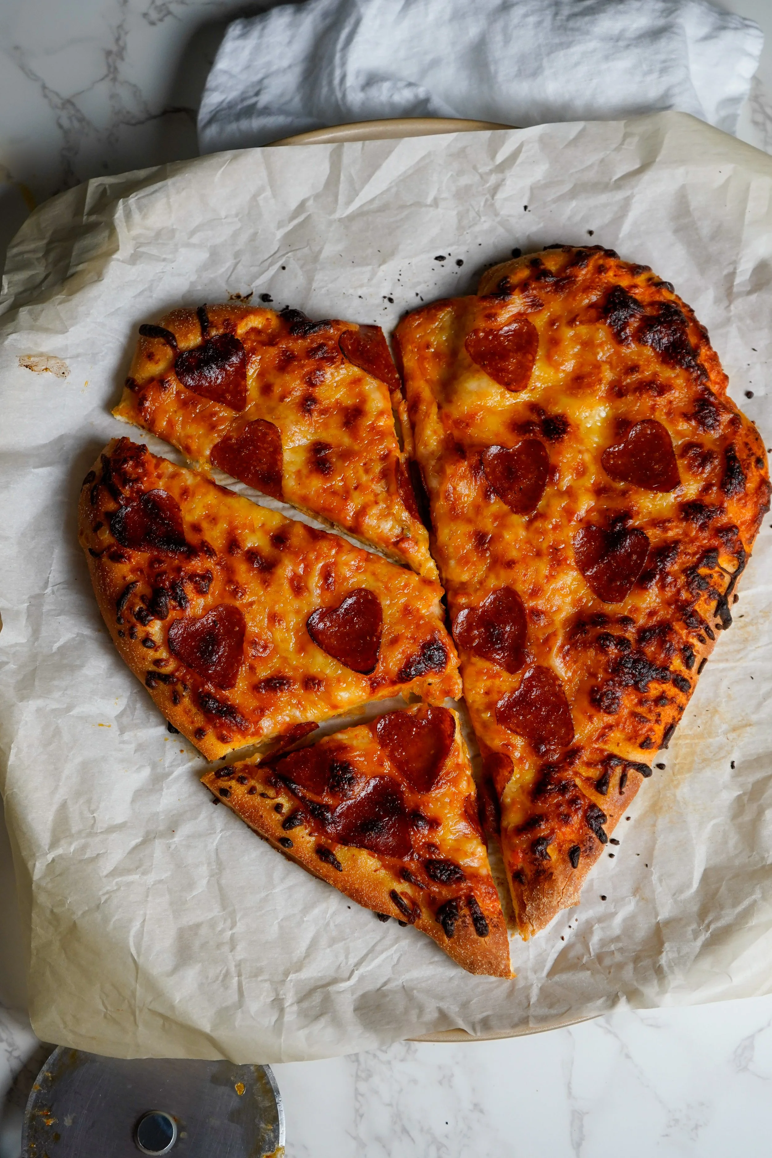 Heart-shaped pepperoni pizza with three slices removed, on a white parchment paper.
