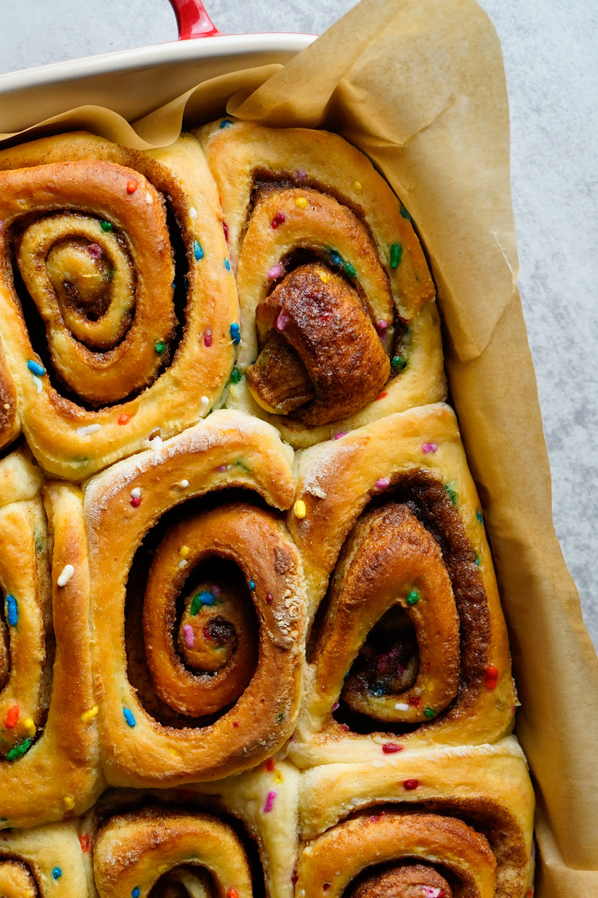 Close-up of freshly baked cinnamon rolls topped with colorful sprinkles in a baking dish.