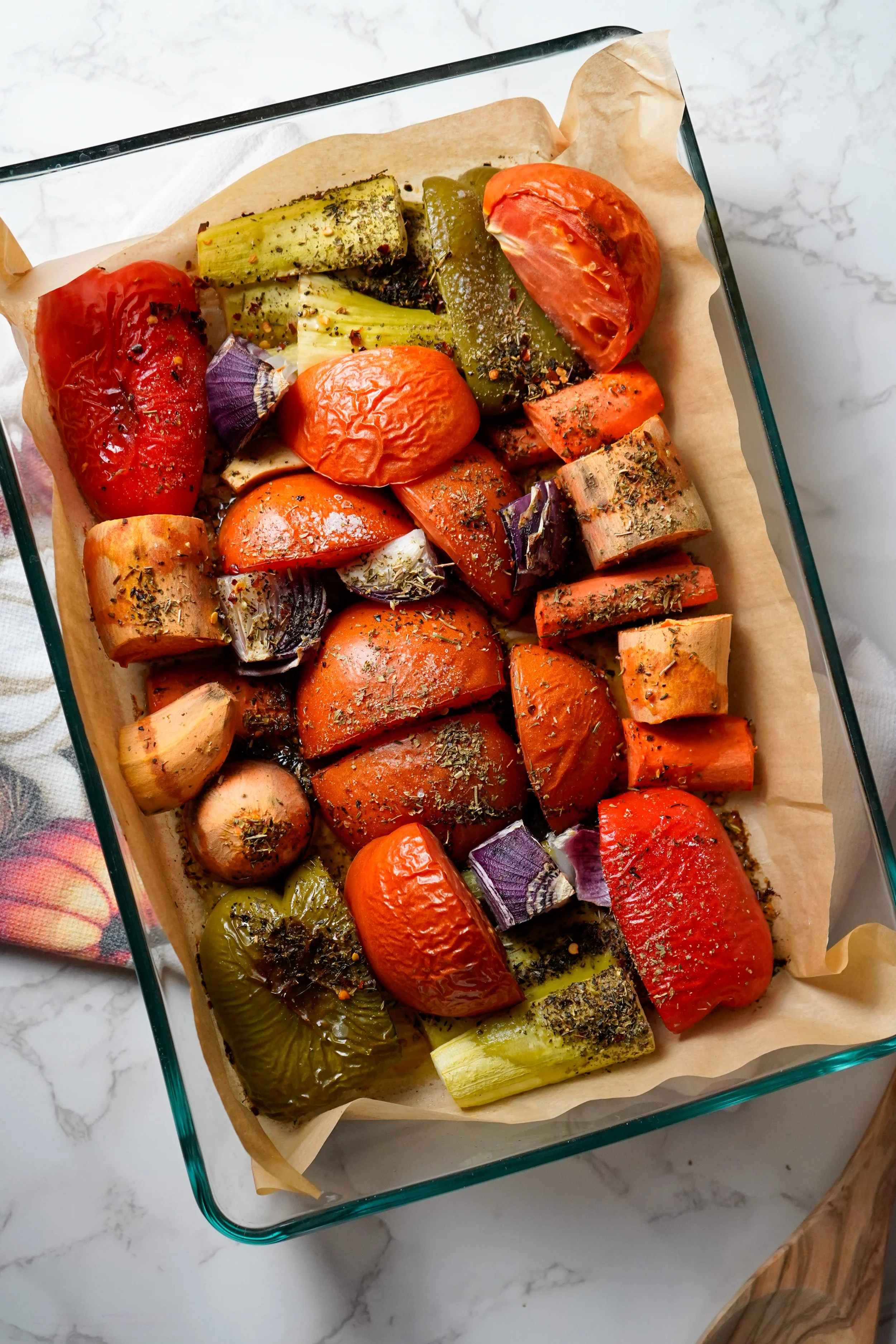 Roasted assorted vegetables on a baking sheet, including tomatoes, zucchini, eggplant, peppers, onions, and carrots, seasoned with herbs and spices.