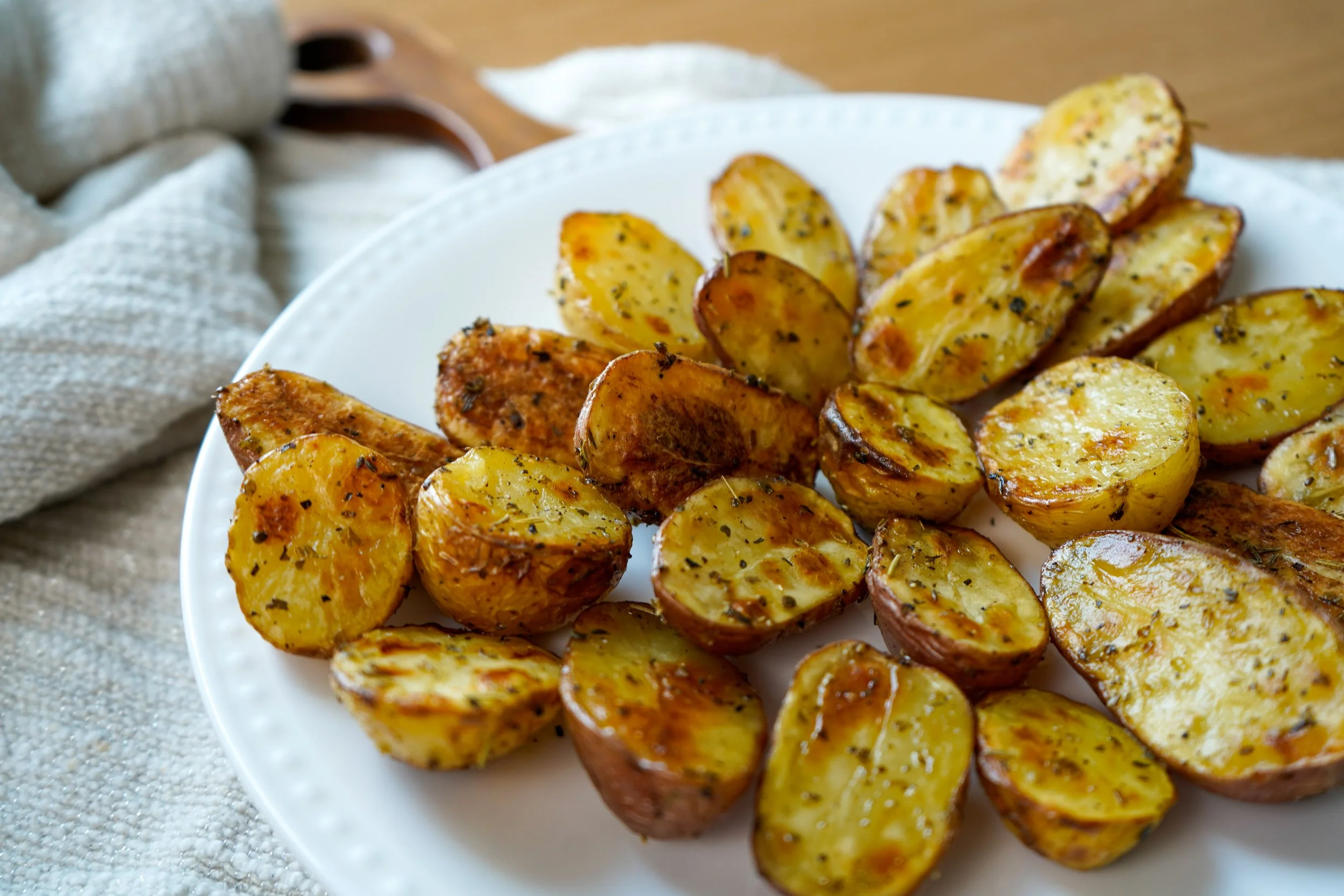 Roasted halved potatoes seasoned with herbs on a white plate.