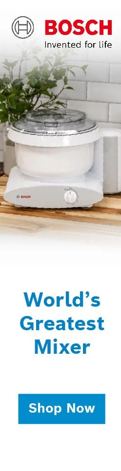 Bosch countertop mixer with a transparent mixing bowl on a kitchen counter next to a plant and white brick wall, advertising as the world's greatest mixer with a shop now button.