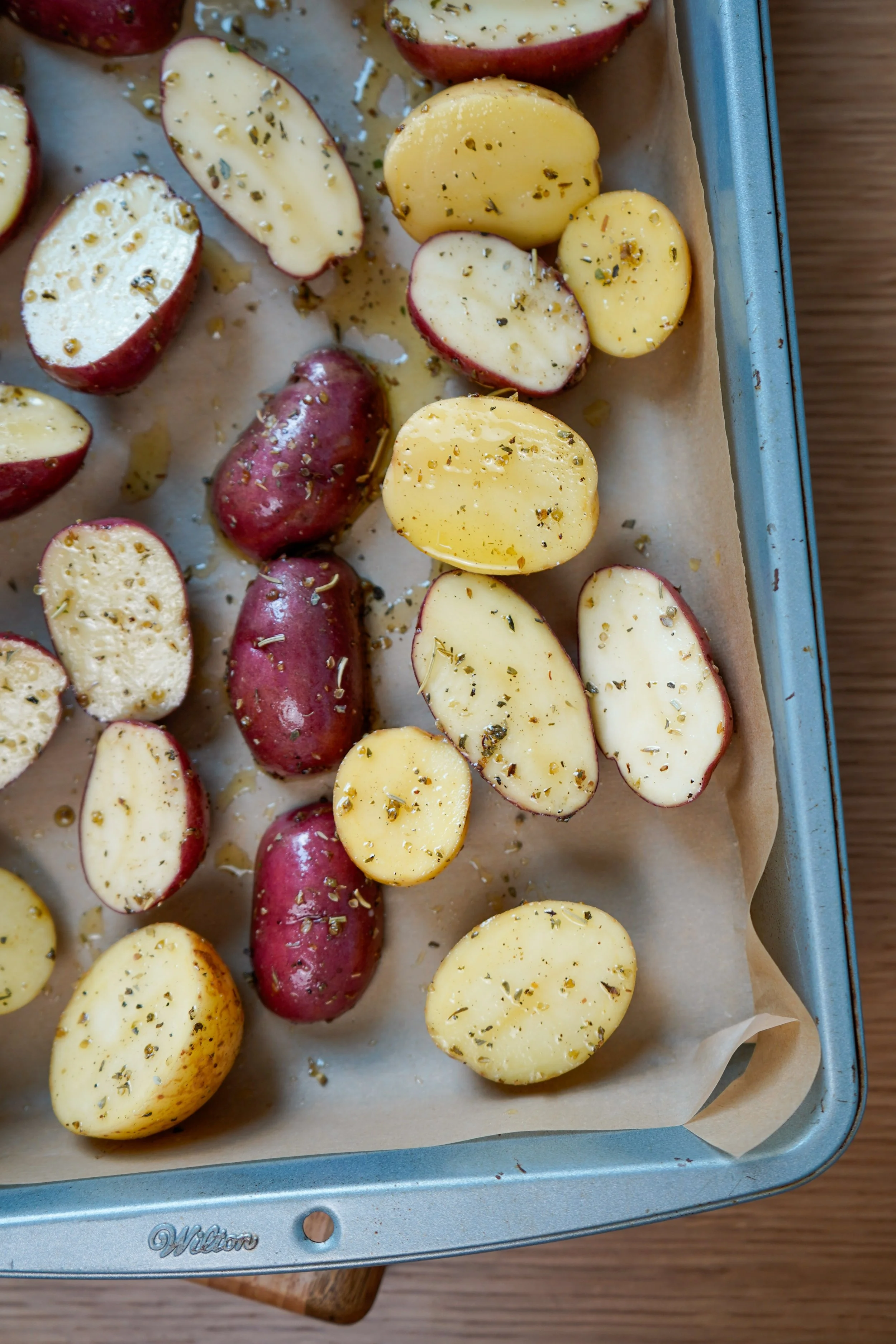 Red and yellow potatoes halved and seasoned with herbs on a baking sheet.
