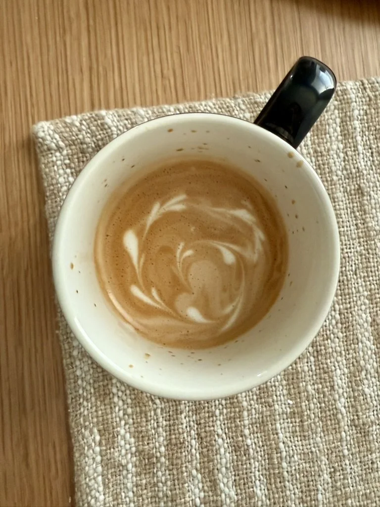 coffee cup with coffee and cream heart swirls, placed on a woven beige napkin on a wooden table.