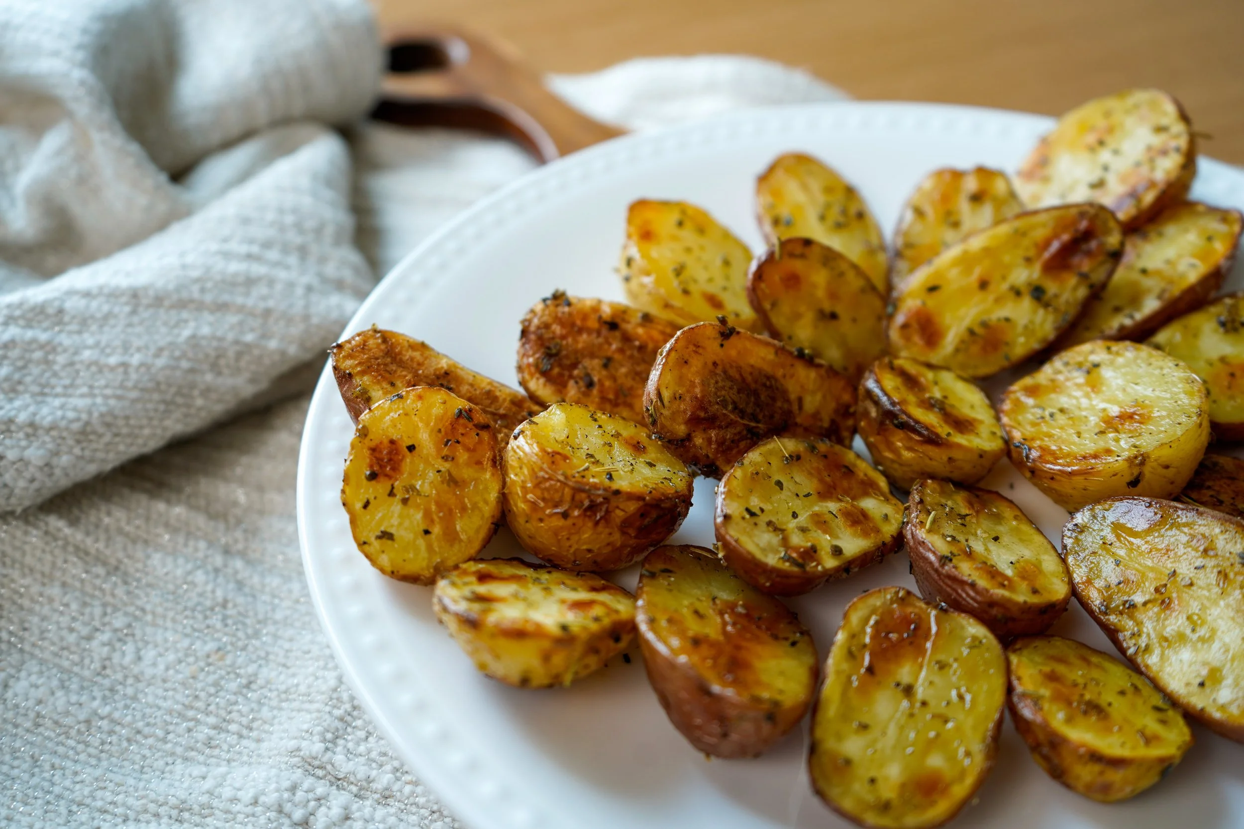 Roasted halved potatoes seasoned with herbs on a white plate