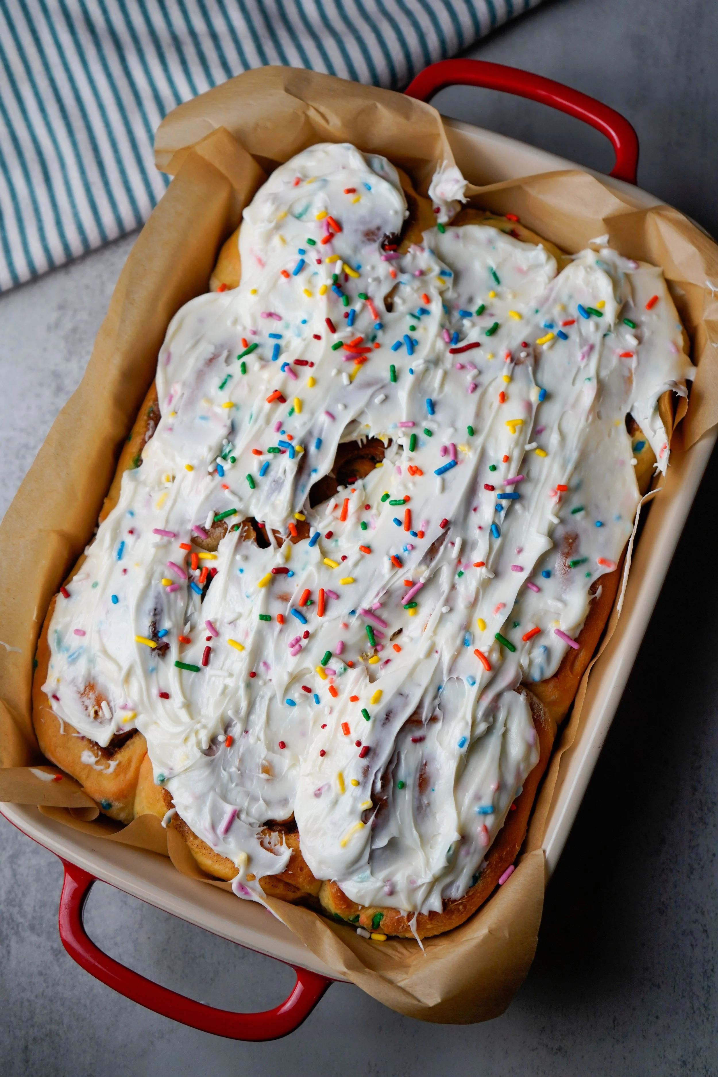 Homemade confetti cinnamon rolls with white frosting and colorful sprinkles in a rectangular dish.