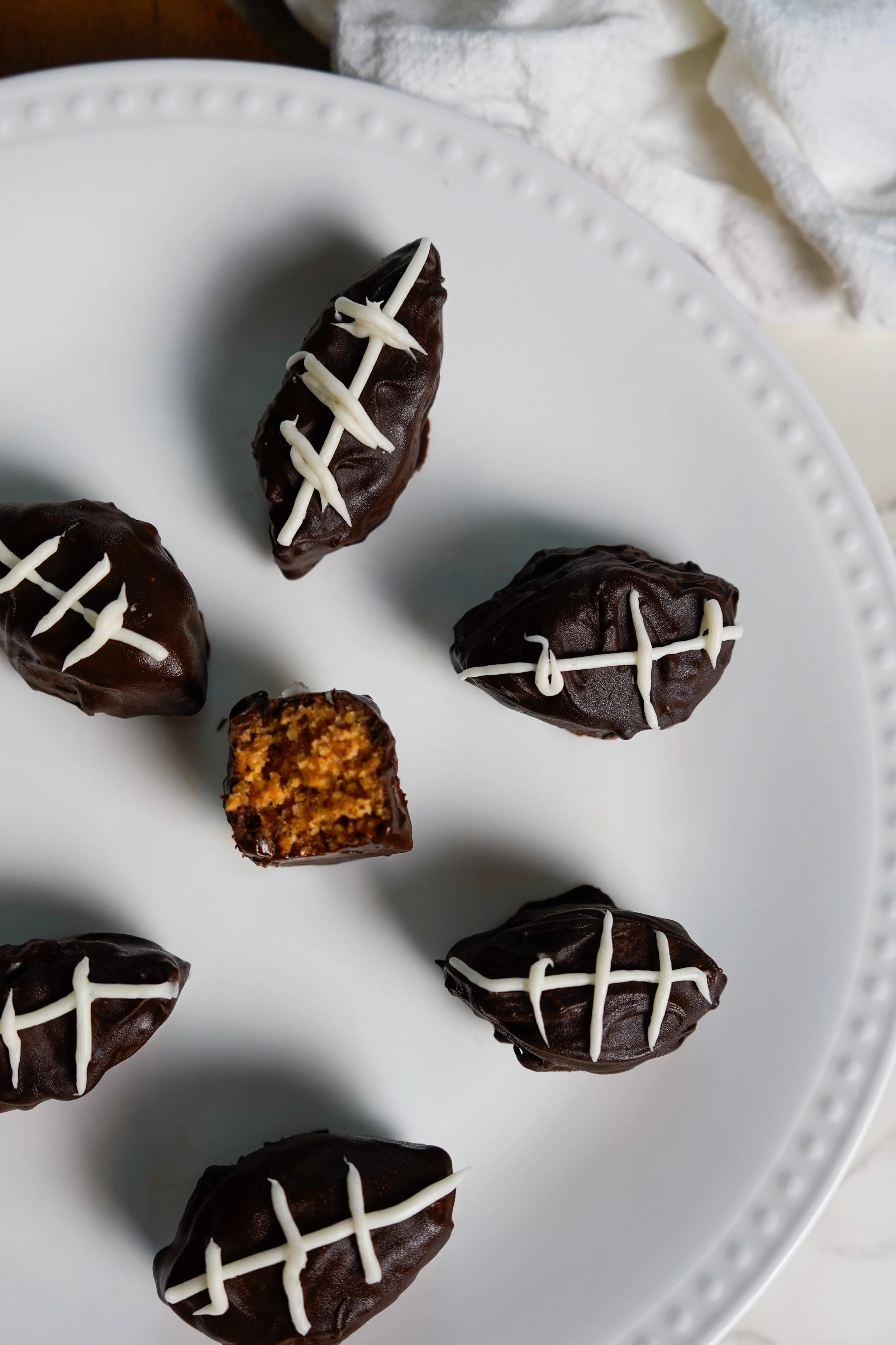 Chocolate-covered footballs with white icing decoration on a white plate.