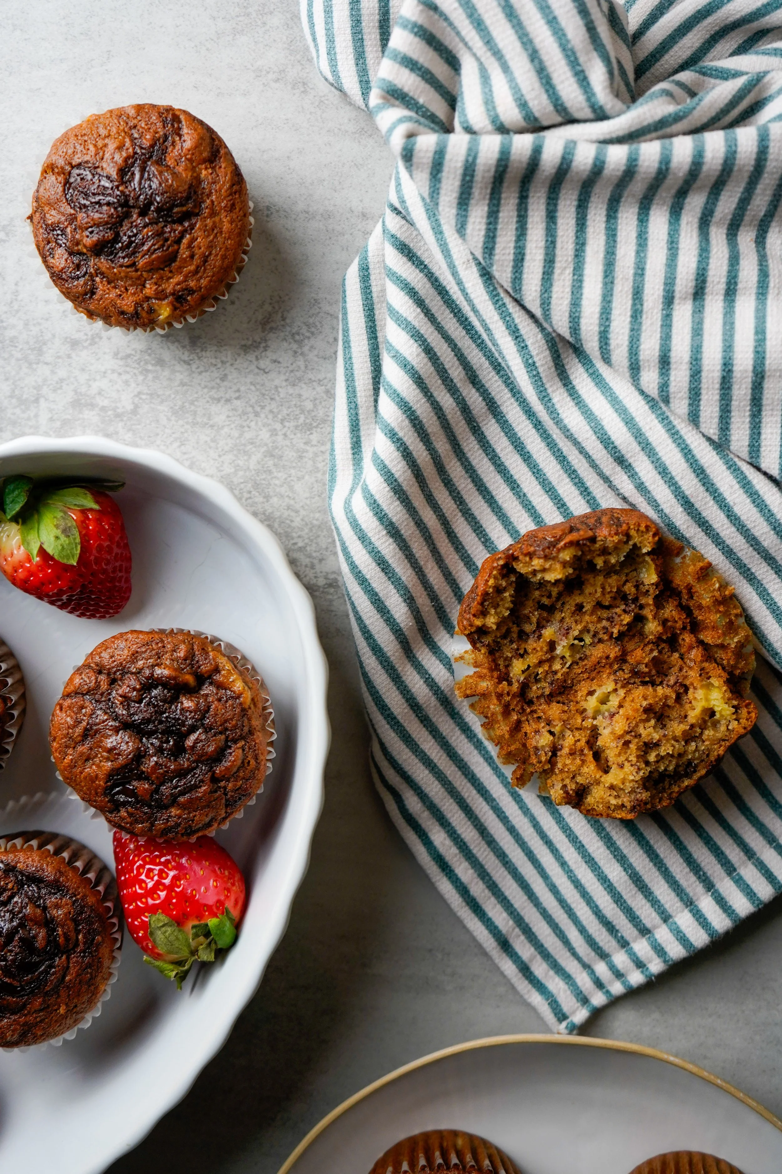 Hazelnut swirl banana muffins with strawberries on a plate and a halved muffin on a striped napkin.