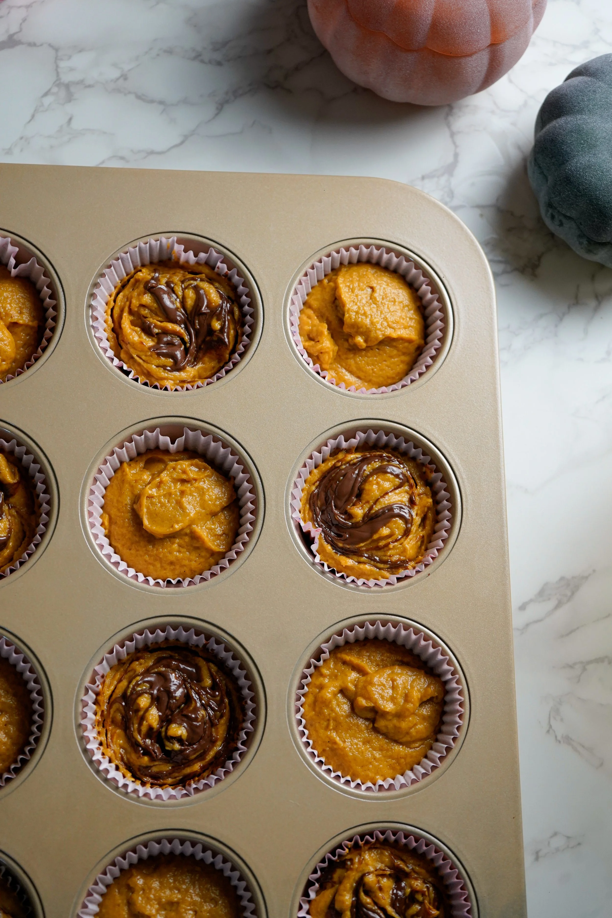 Nine unbaked cupcakes in a metal baking tray, with a hazelnut swirl on top.