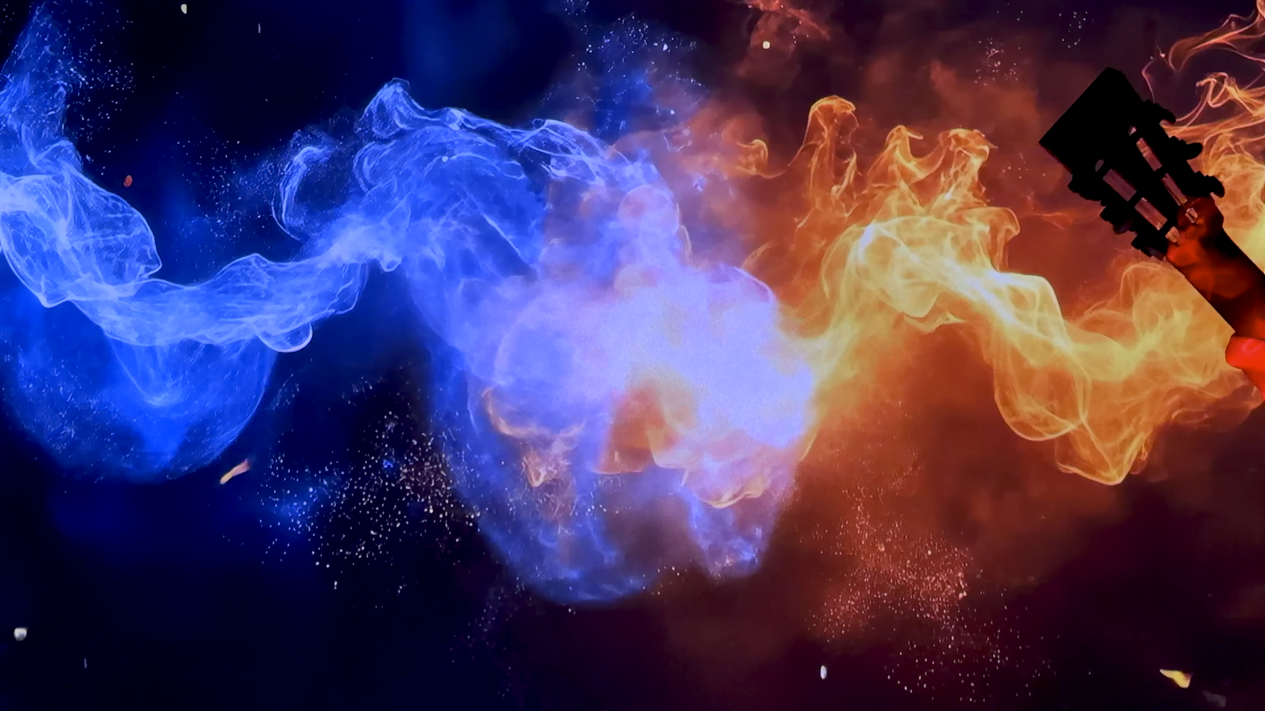 Colorful blue and orange flames or smoke swirling against a dark background, with a silhouette of a person or object at the right side.