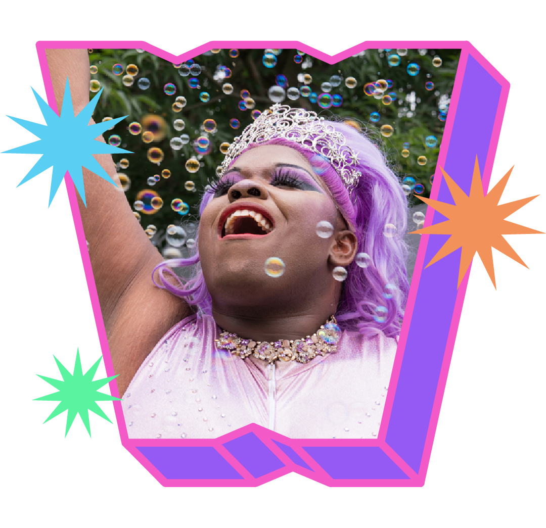 Lavender, a drag queen wearing a tiara and a purple dress, sings while pointing an arm straight up into the air