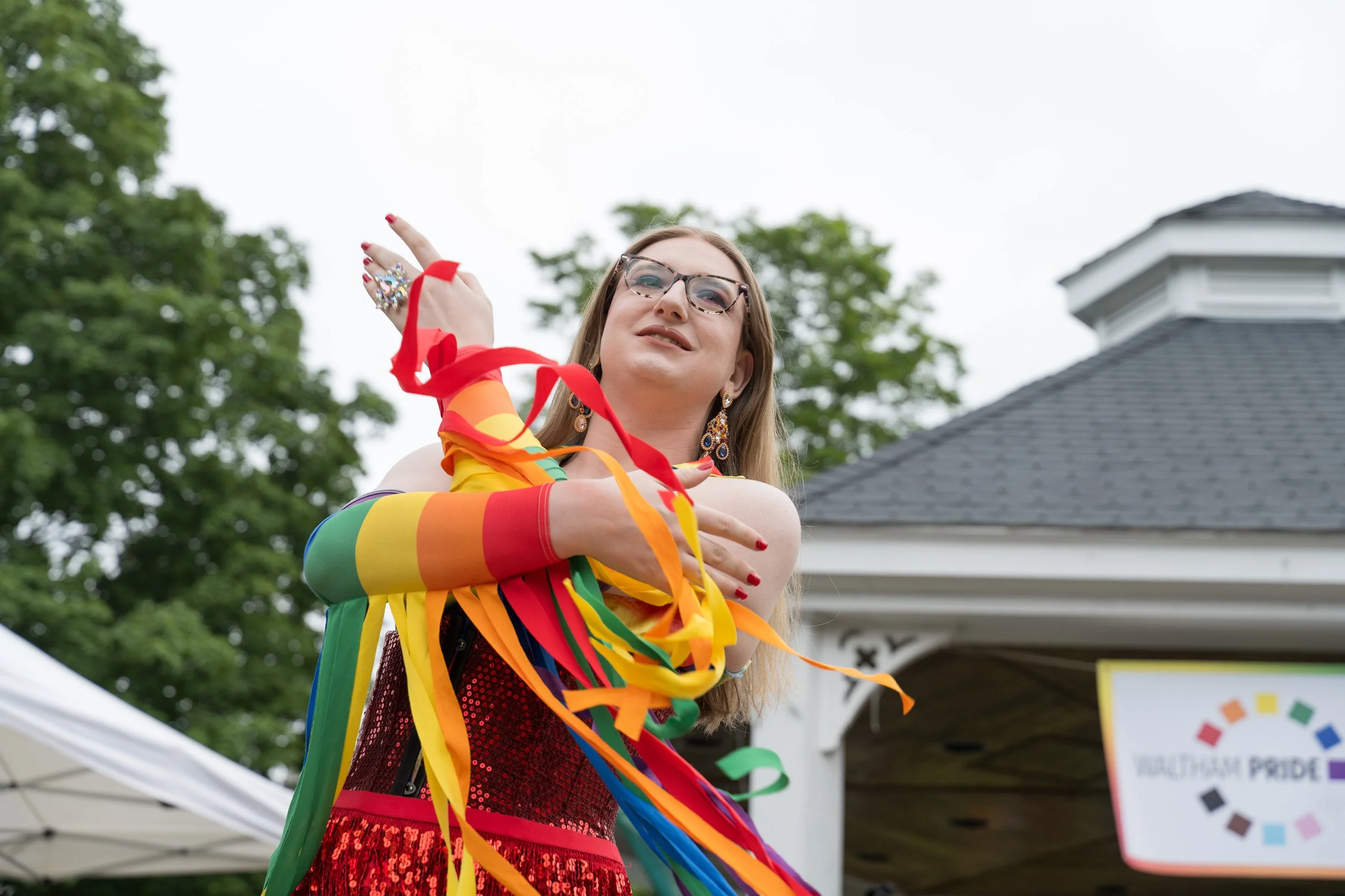 A drag queen wearing red, sparkly dress dances with rainbow ribbons