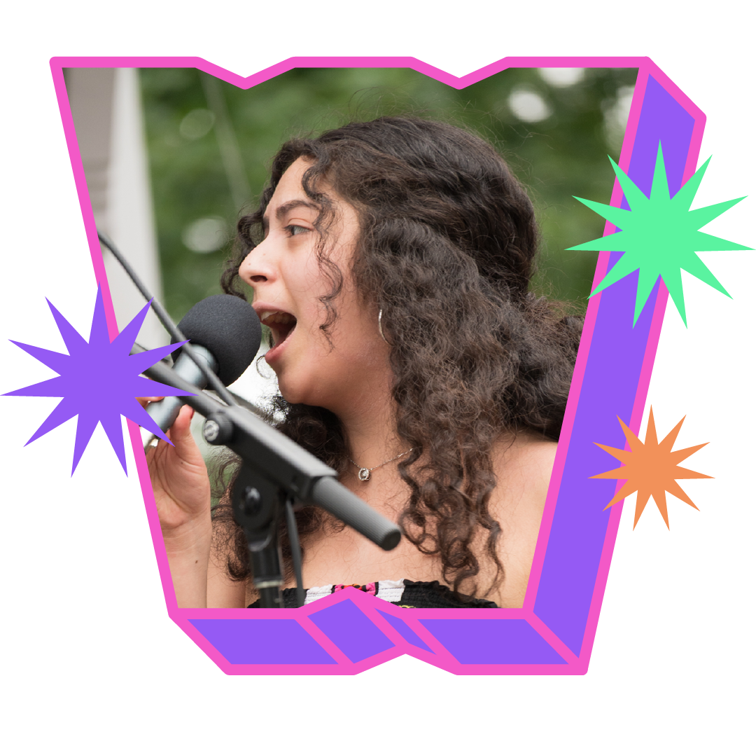 Mara Morales, with dark, wavy should blade length hair, sings into a microphone