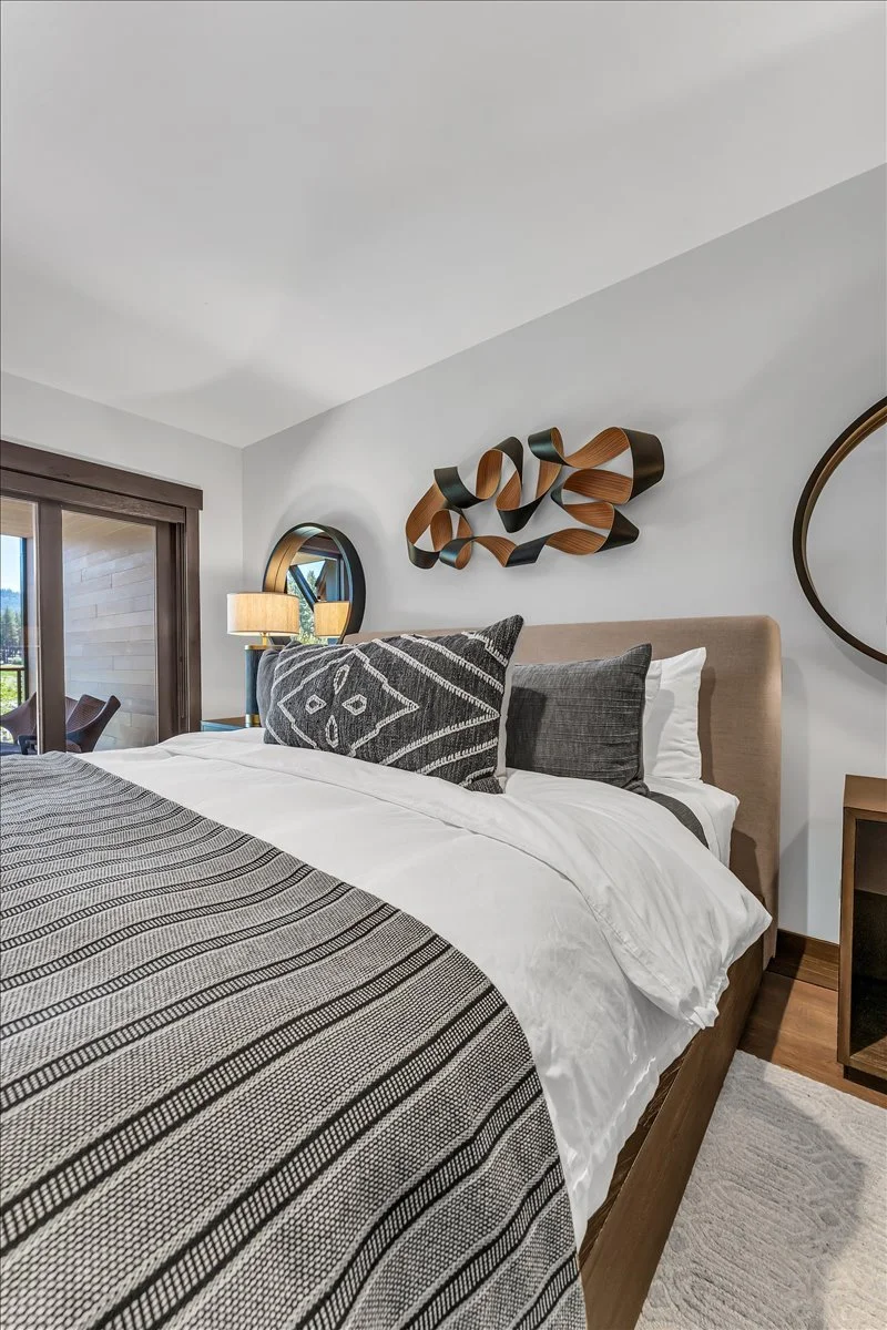 This elegantly designed  bedroom features contemporary design with warm wood furnishings and expansive windows, while glass doors open to a private patio, allowing abundant natural light to brighten the space and create a comfortable, welcoming atmos