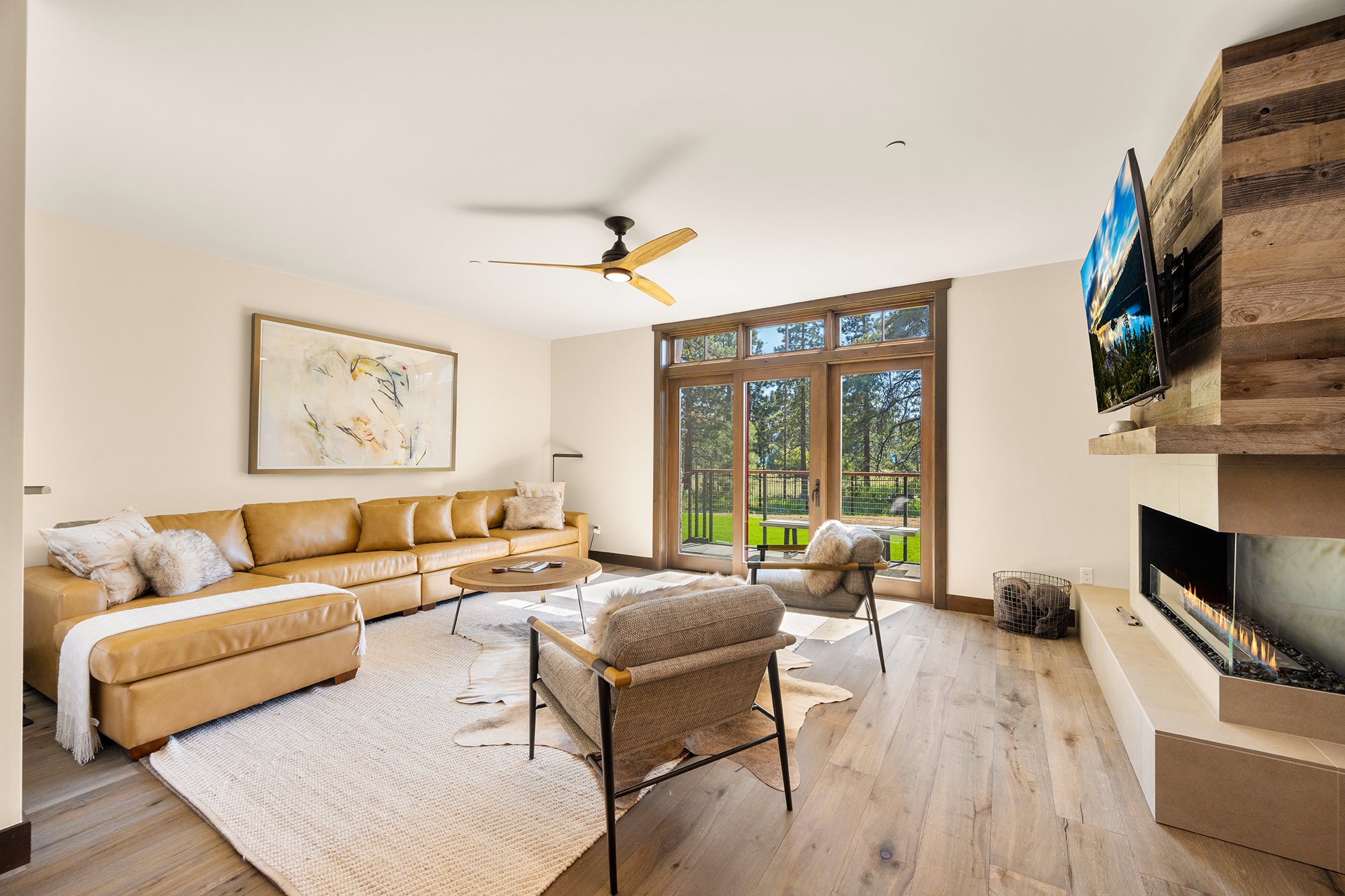 A spacious living room with a cozy couch, a warm fireplace, and a ceiling fan. Glass doors open up to a patio overlooking Tahoe Beach Club. 