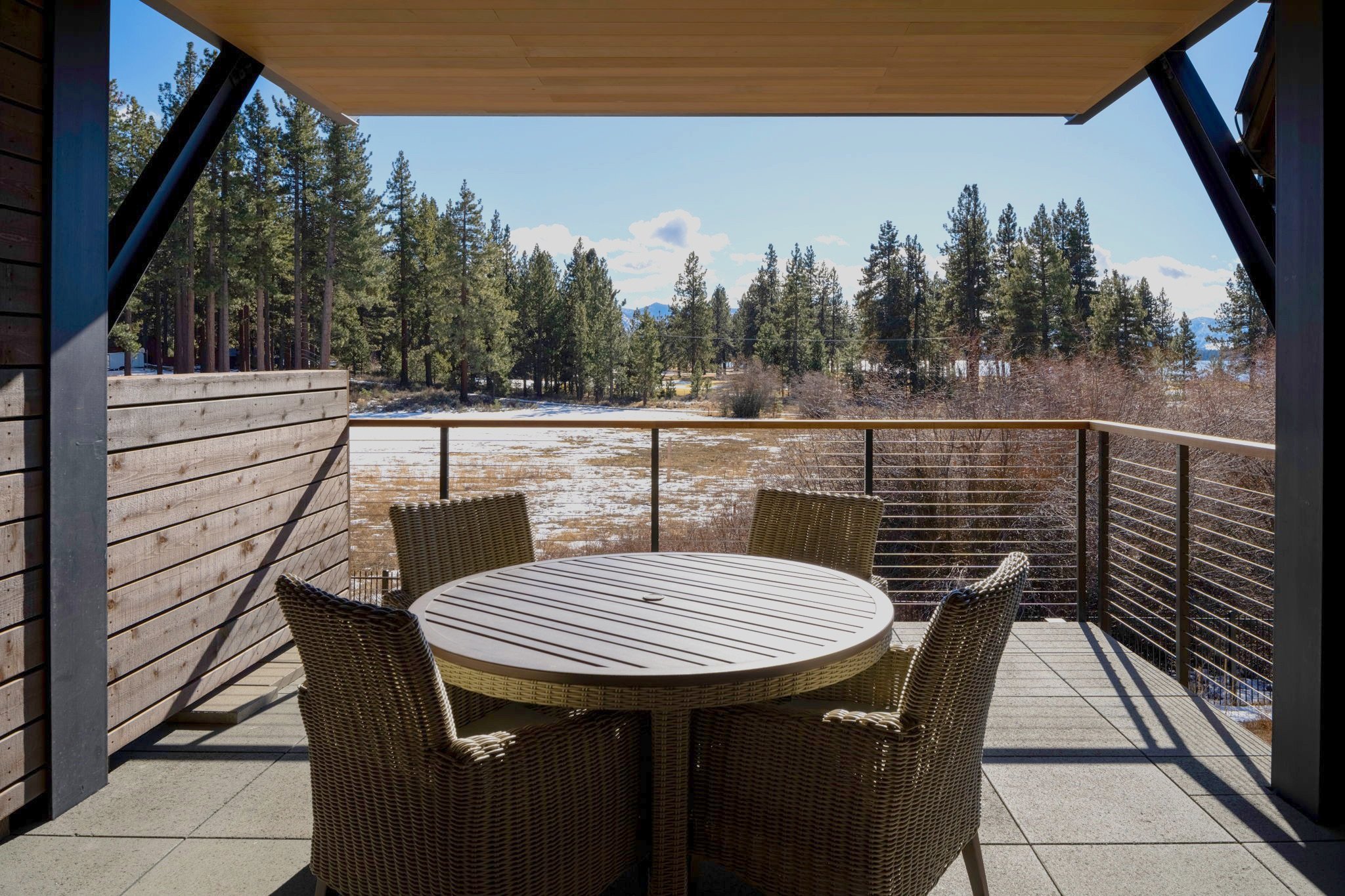 A cozy patio with a wooden table and chairs, with a view of Lake Tahoe and the surrounding greenery. 