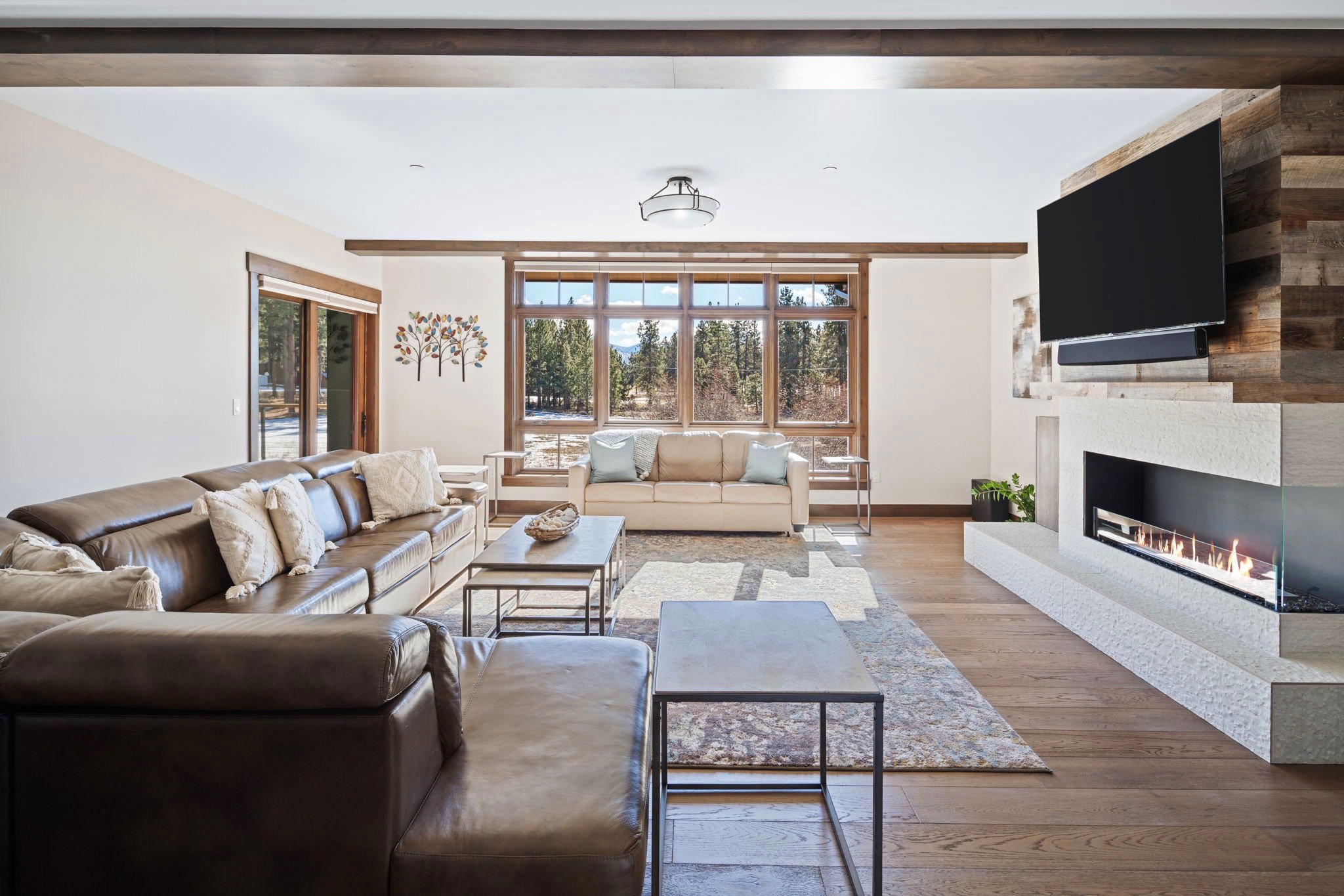 A cozy living room with a fireplace crackling warmly and a flat-screen TV. Glass doors open up to the Tahoe landscape. 