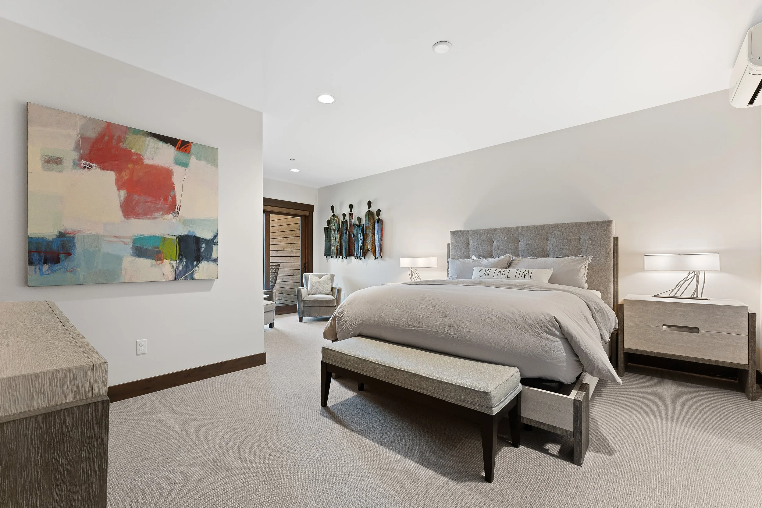 Contemporary and bright bedroom featuring a large bed, bright carpet, with a door opening to a private patio