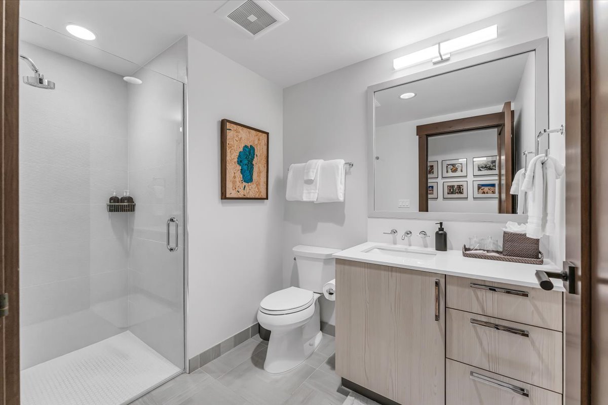 This luxurious bathroom showcases a stylish vanity, a mirror, and light wood cabinetry, beautifully complemented by an enclosed glass shower with custom tiles.