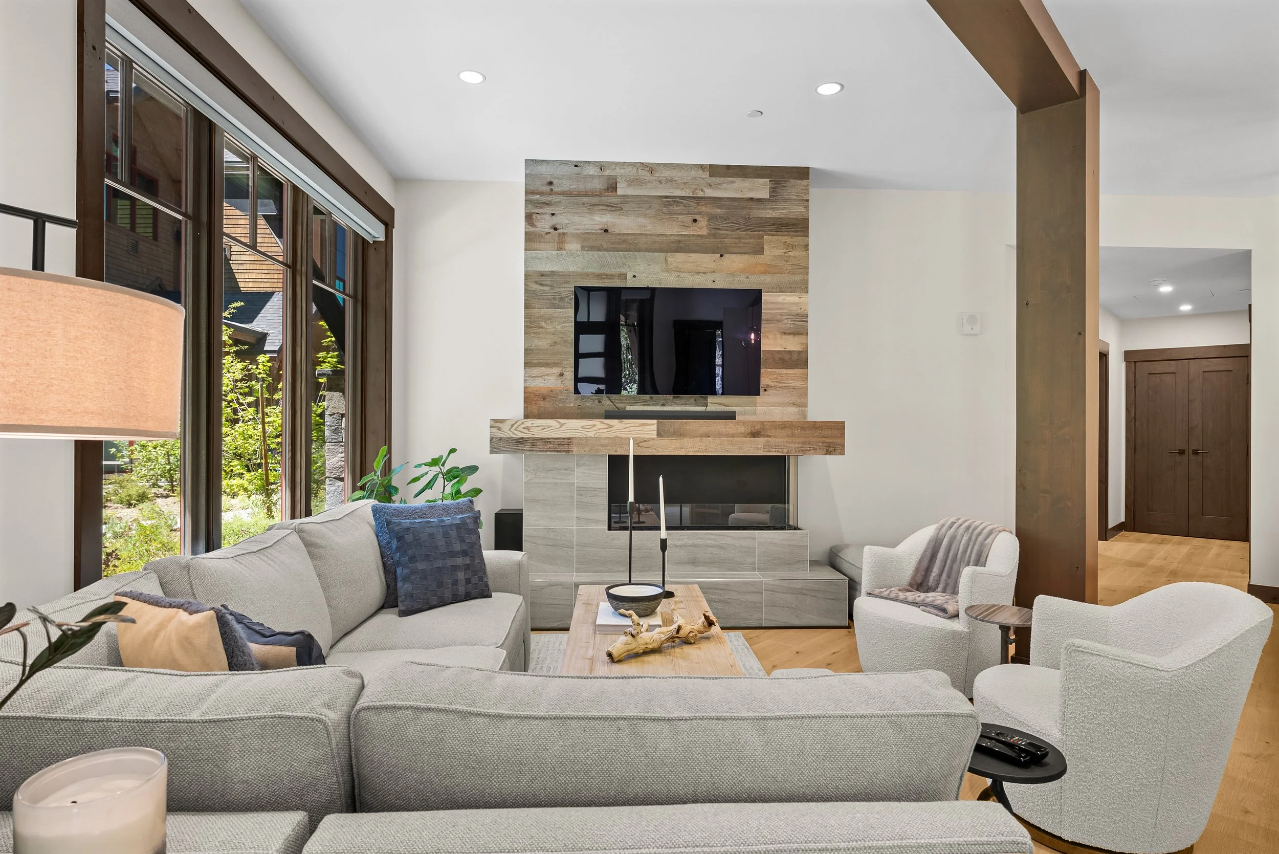 Cozy Tahoe Beach Club living room with a large sectional sofa, stone fireplace, and expansive windows overlooking the surrounding forest.