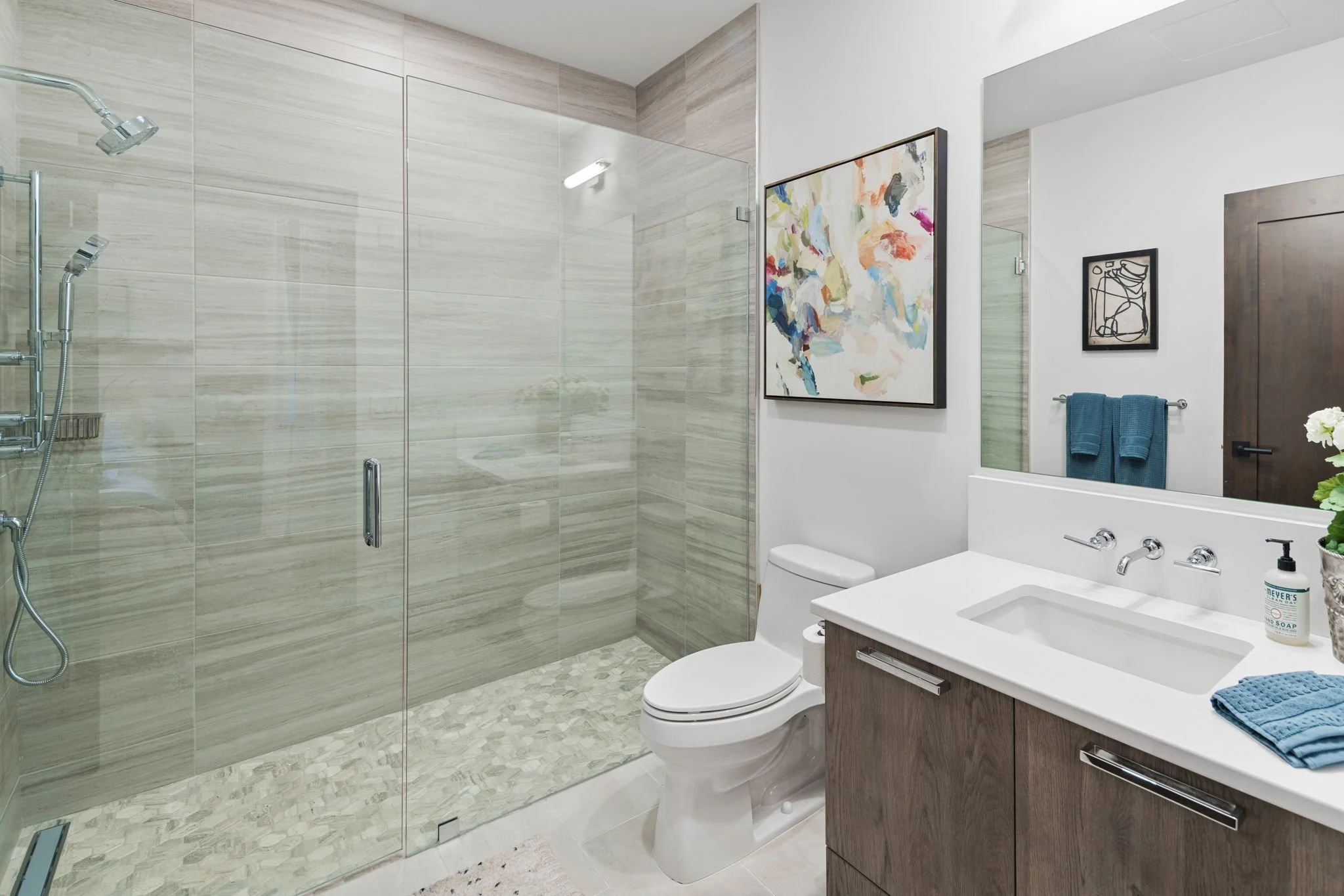Spacious Bathroom with Double Vanity, Glass-Enclosed Shower, and Custom Stone Tiles