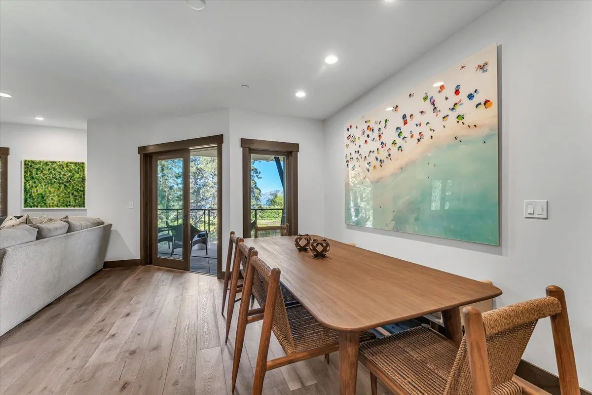 This inviting dining area features a spacious wood dining table, hardwood floors and expansive windows frame picturesque meadow views, while glass doors provide seamless access to a private patio.