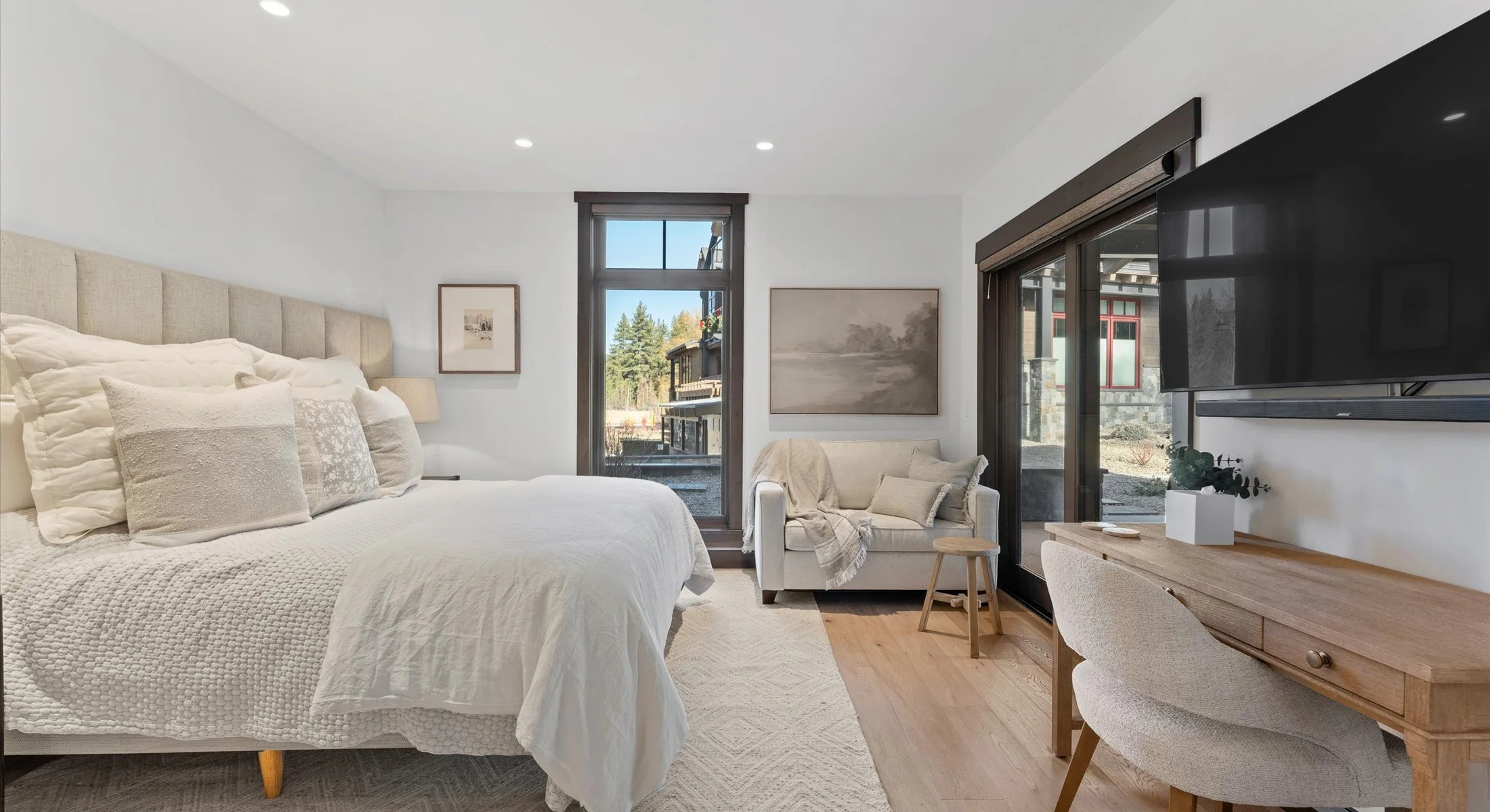One of Residence 111's three bedrooms, serenely decorated, showcasing a cozy bed, a practical desk, a mounted television and doors leading out to a private patio.