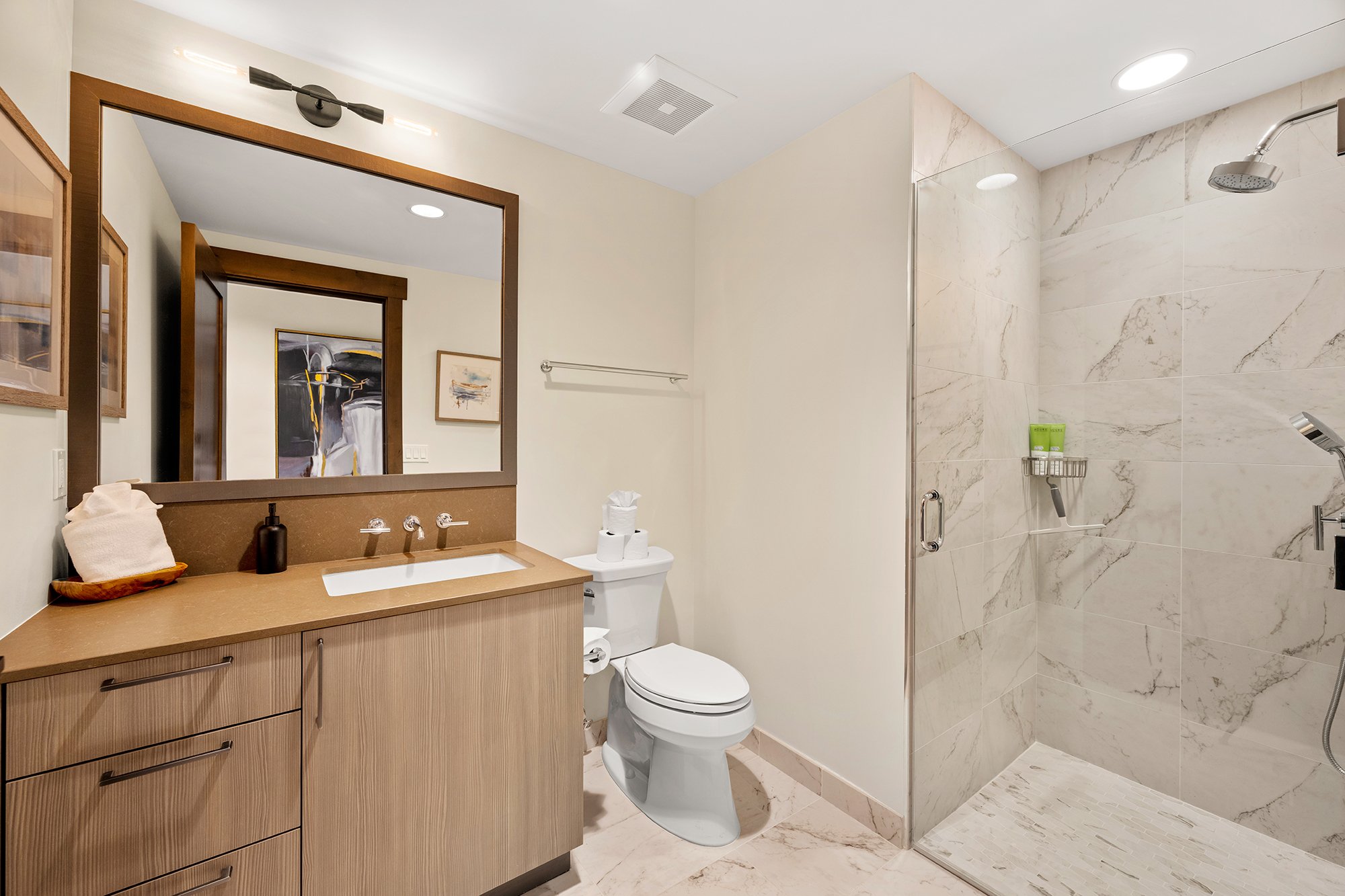 A modern bathroom featuring a sleek shower, a toilet, and a large vanity with sink.