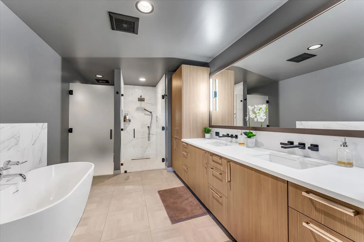 Residence 219 features a spa-inspired bathroom with a double vanity, glass-enclosed shower, freestanding soaking tub, and custom stone flooring.
