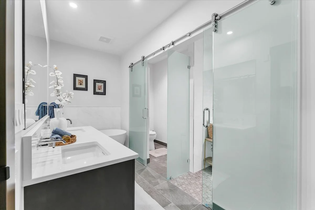 This modern bathroom features a large double sink vanity with custom tile flooring and glass enclosed shower 